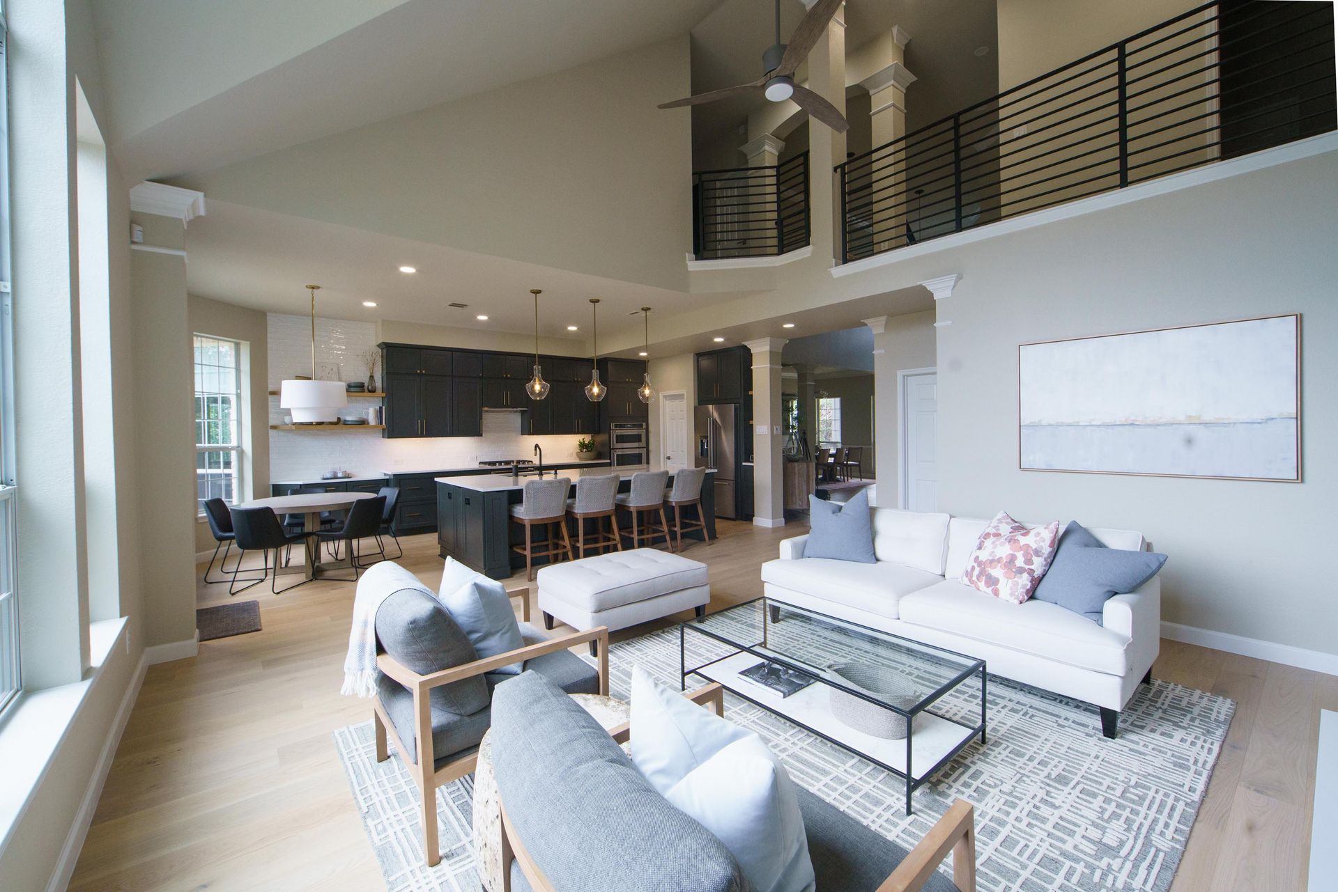 Open-concept living space with kitchen and seating areas; light wood floors, neutral walls, and a loft area.