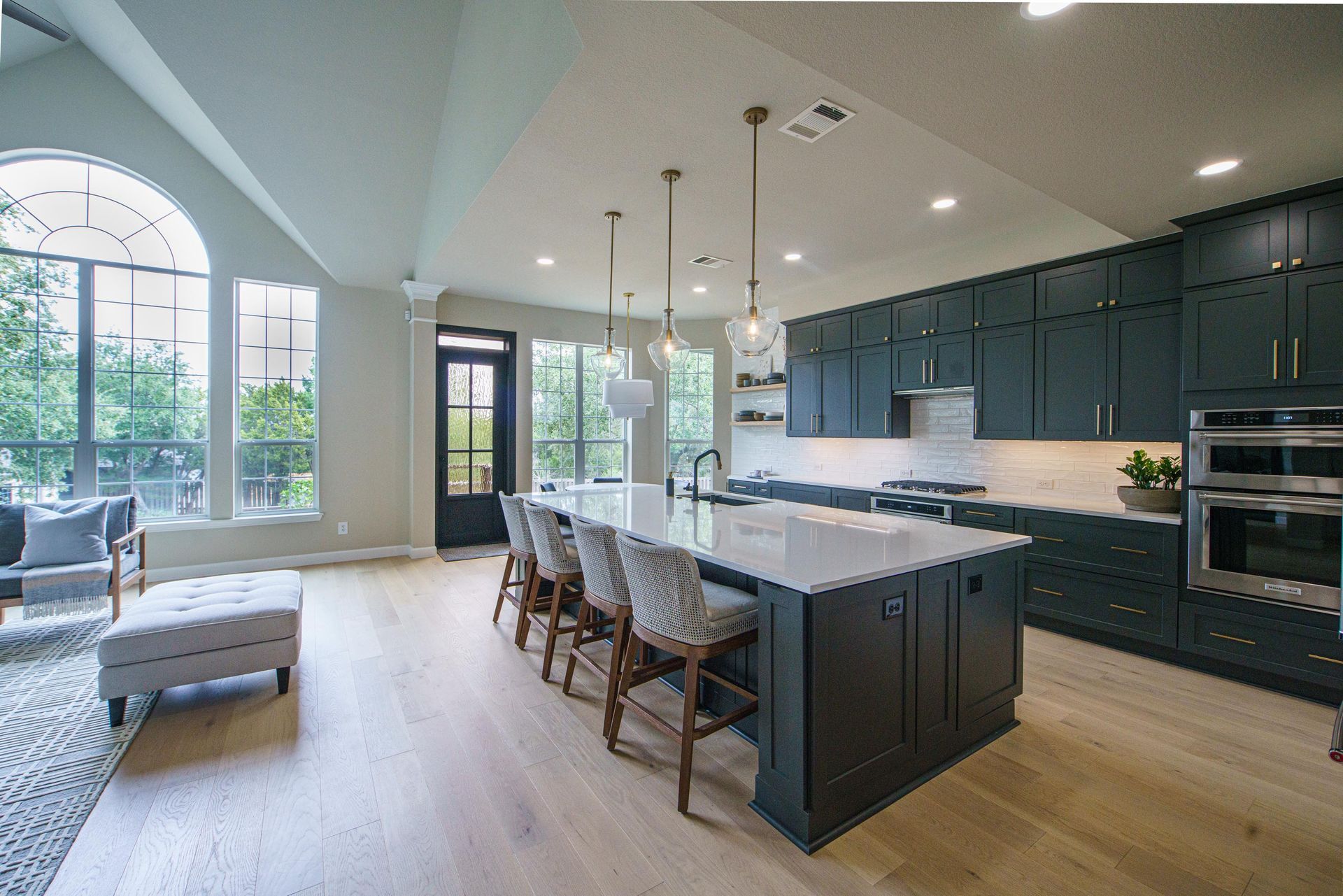 Modern kitchen with dark blue cabinets, large island with seating, and arched window.