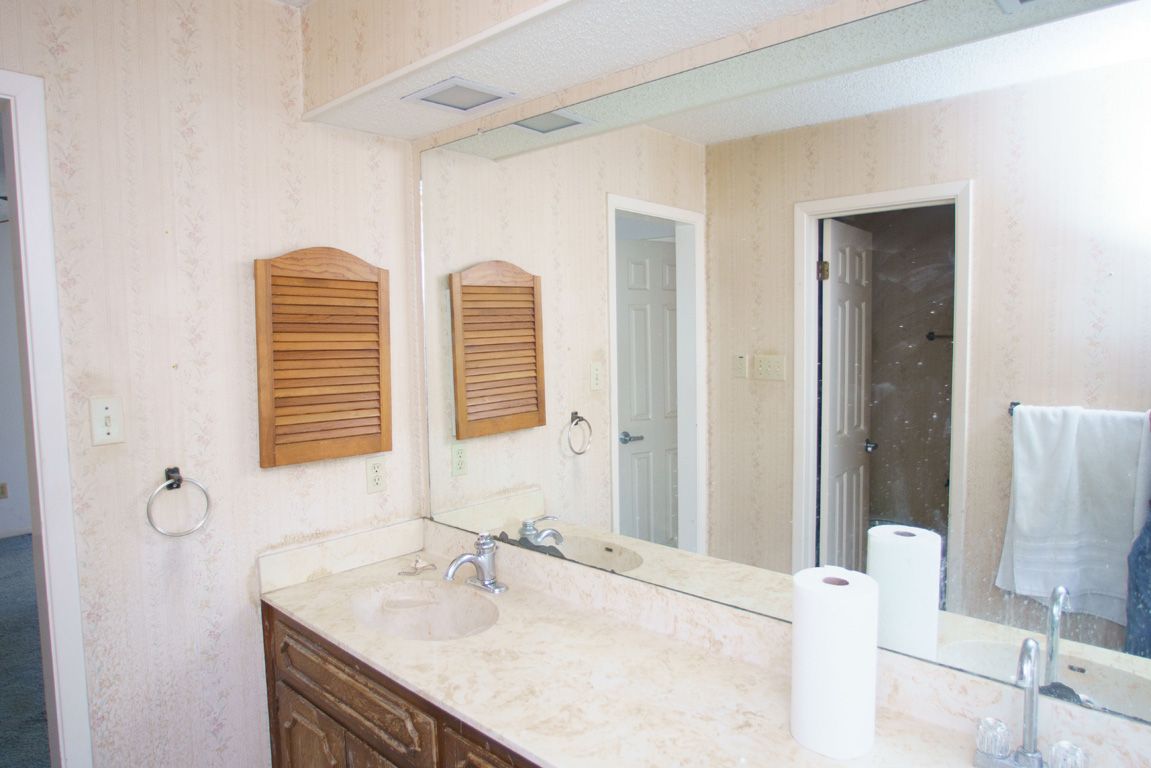 Bathroom with vanity, mirror, two wooden cabinets, and two doorways. Beige walls and counter.