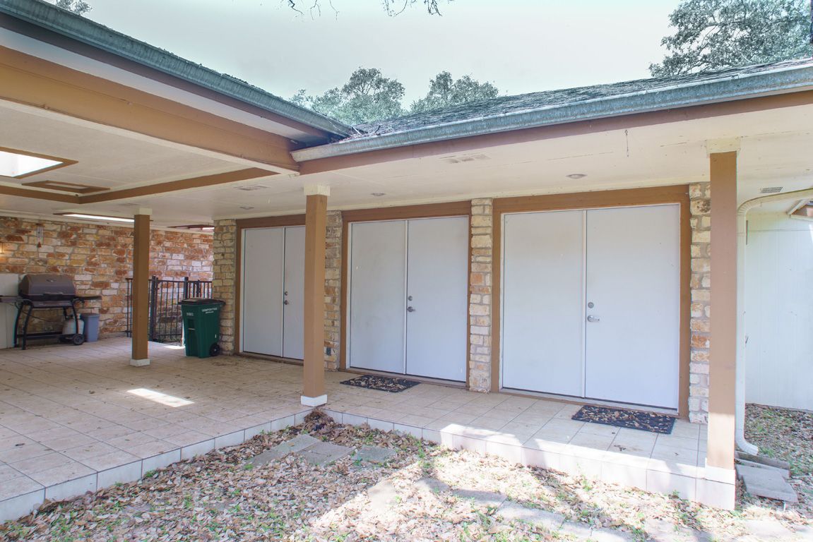 Covered patio with three white doors, stone accents, and a grill.