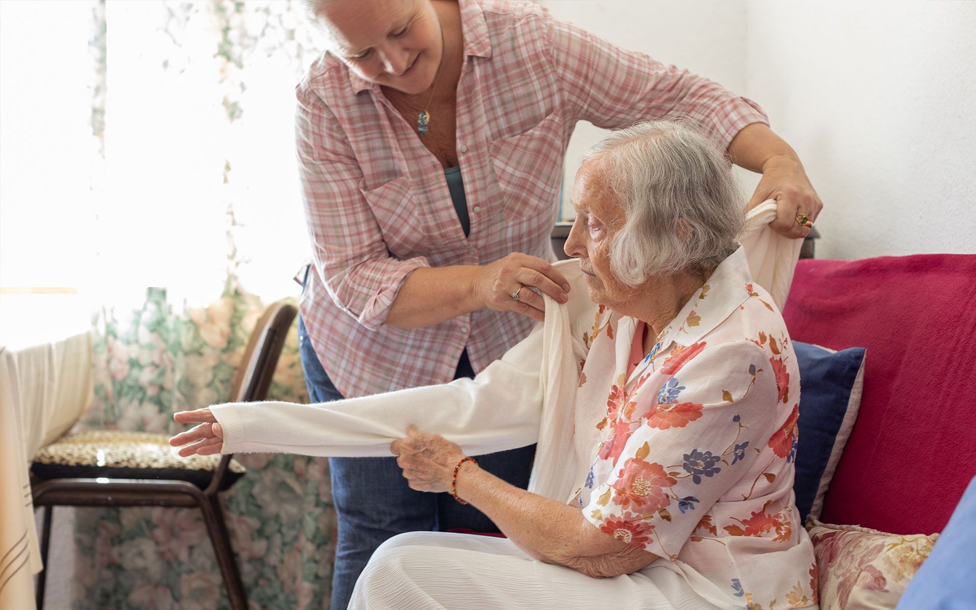 An elderly woman is sitting on a couch being helped by a woman.
