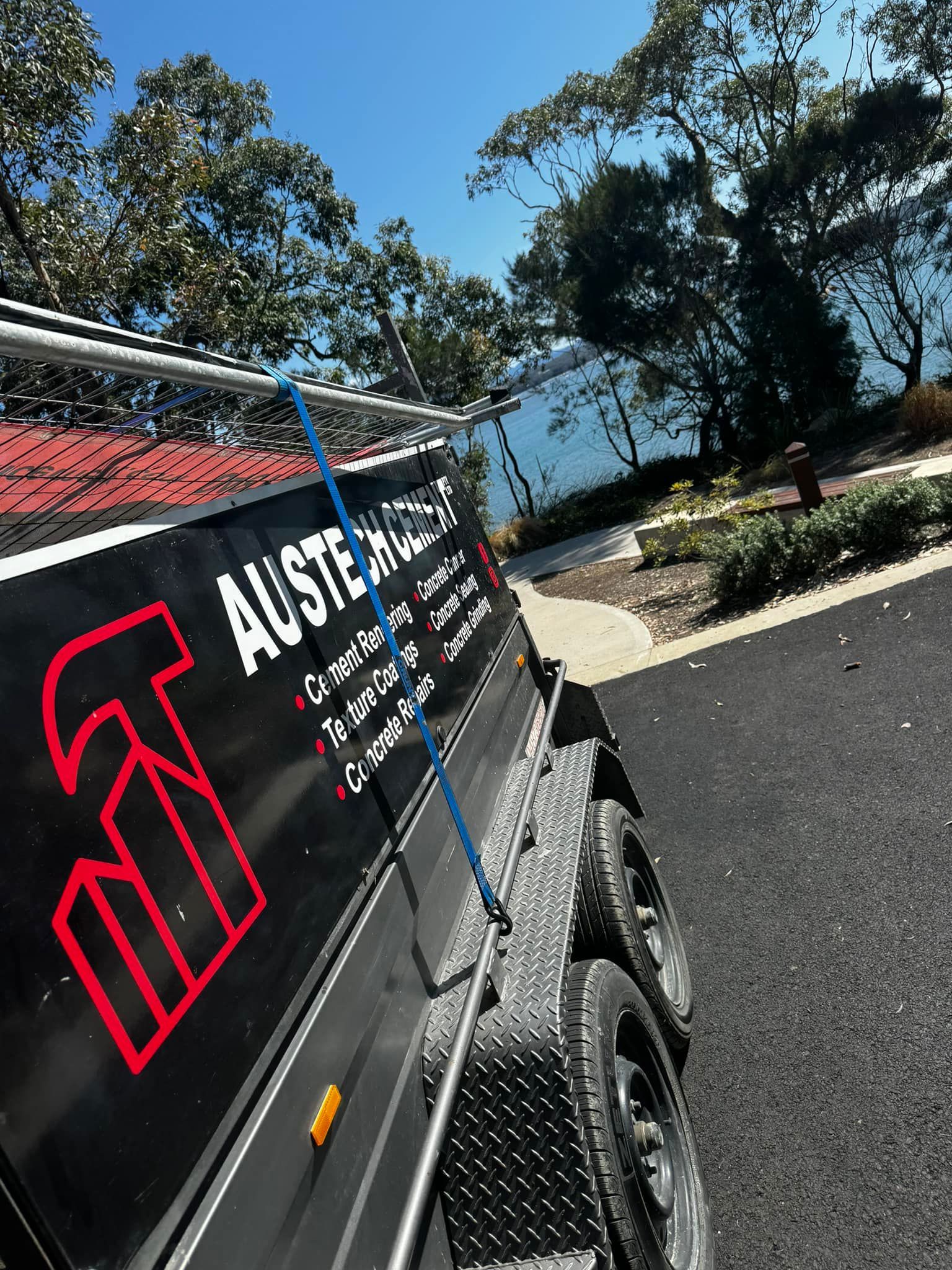 Black utility truck with Austech Cement logo parked on a sunny roadside on the South Coast near trees and water.