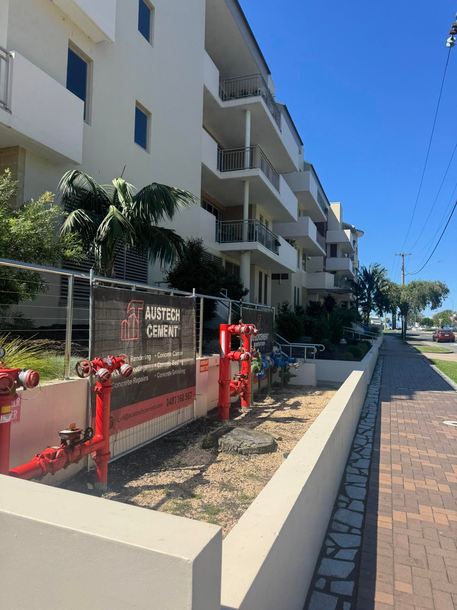 Apartment building walkway with Austech Cement banner on the south coast and a sunny blue-sky sidewalk.
