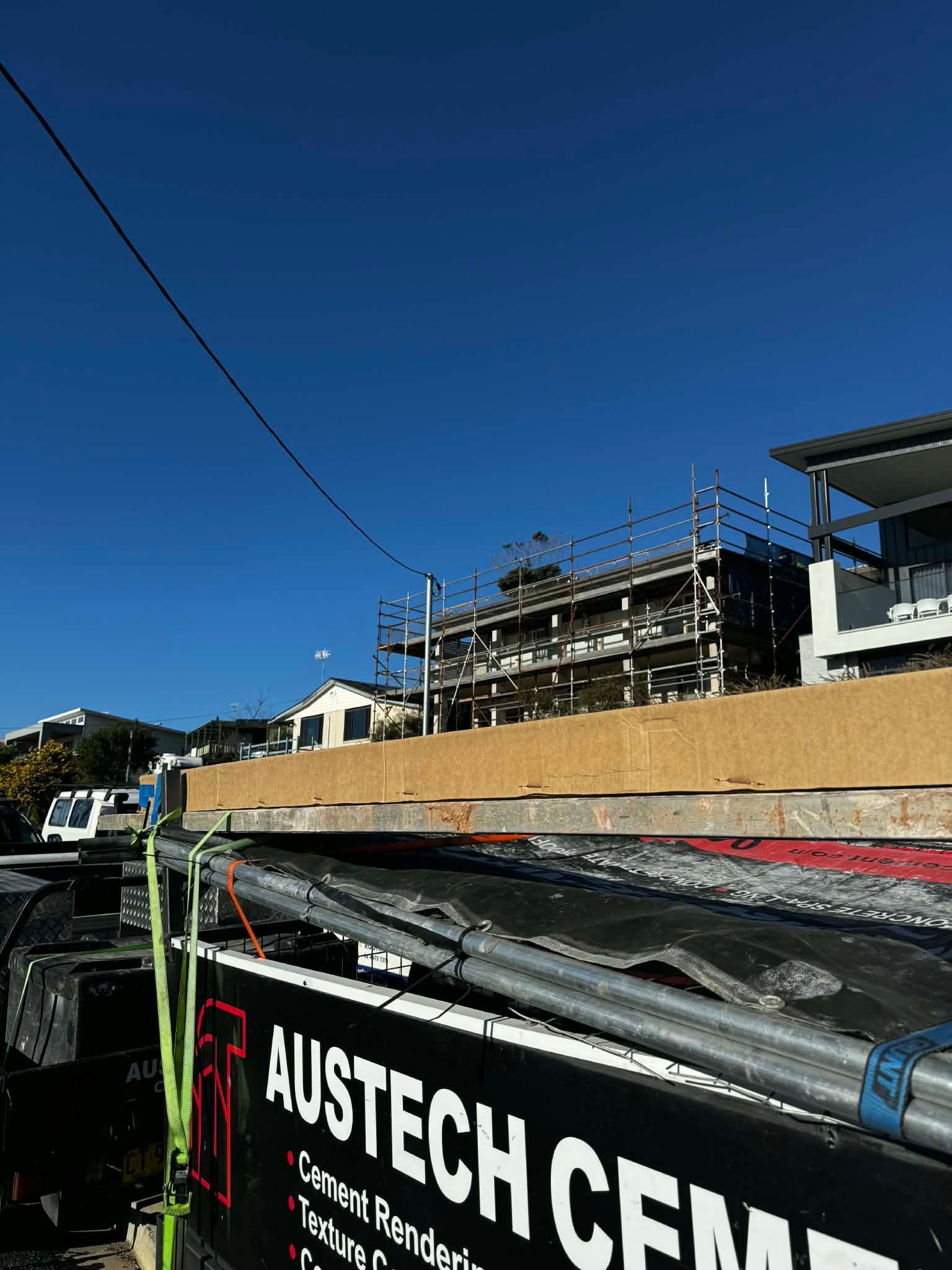 Construction site with scaffolding and a concrete wall under a clear blue sky, with AUSTECH banner in foreground