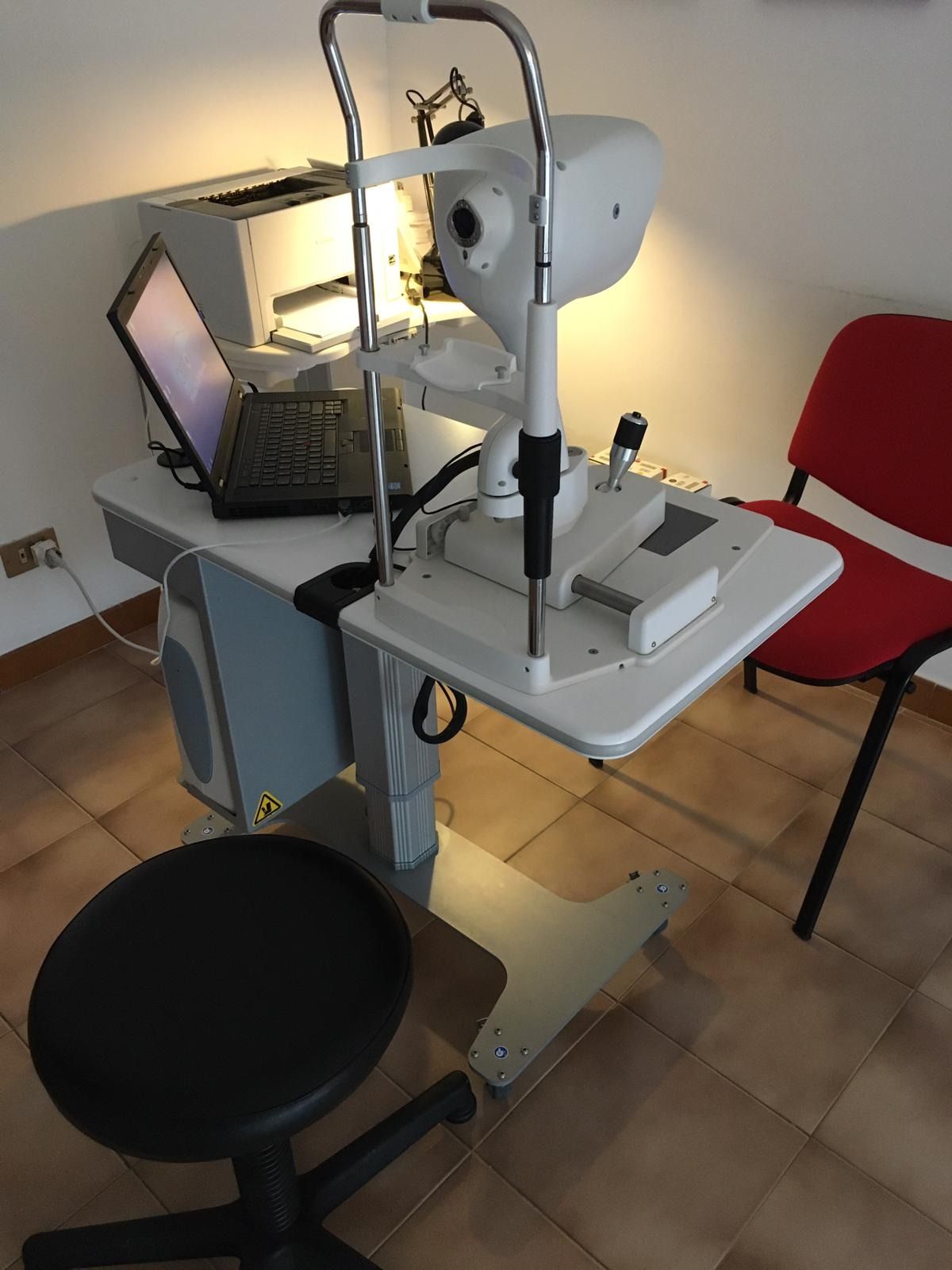 Attrezzatura per esami oculistici con un computer portatile e uno sgabello nero 