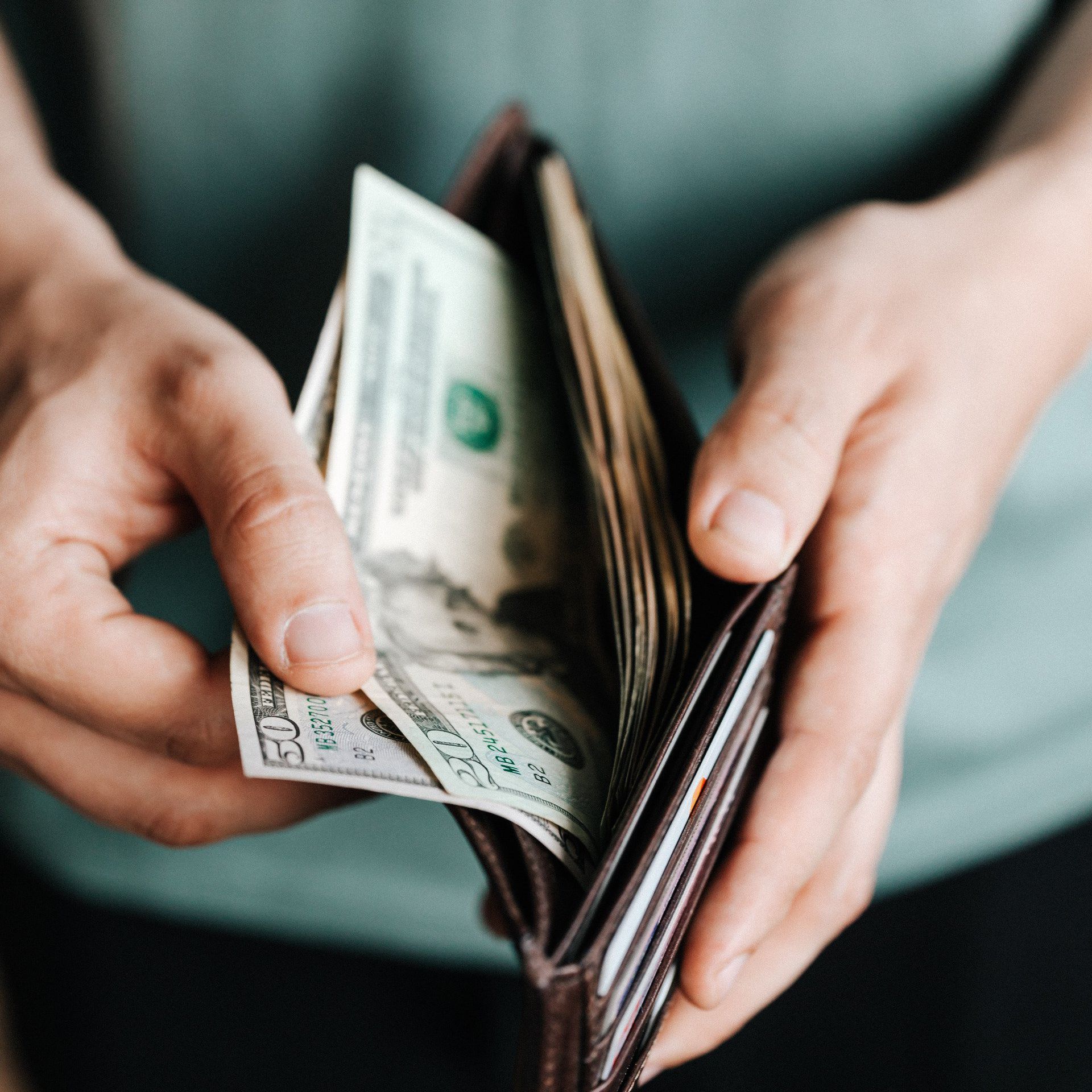 a person is taking money out of a wallet that has a 50 dollar bill in it
