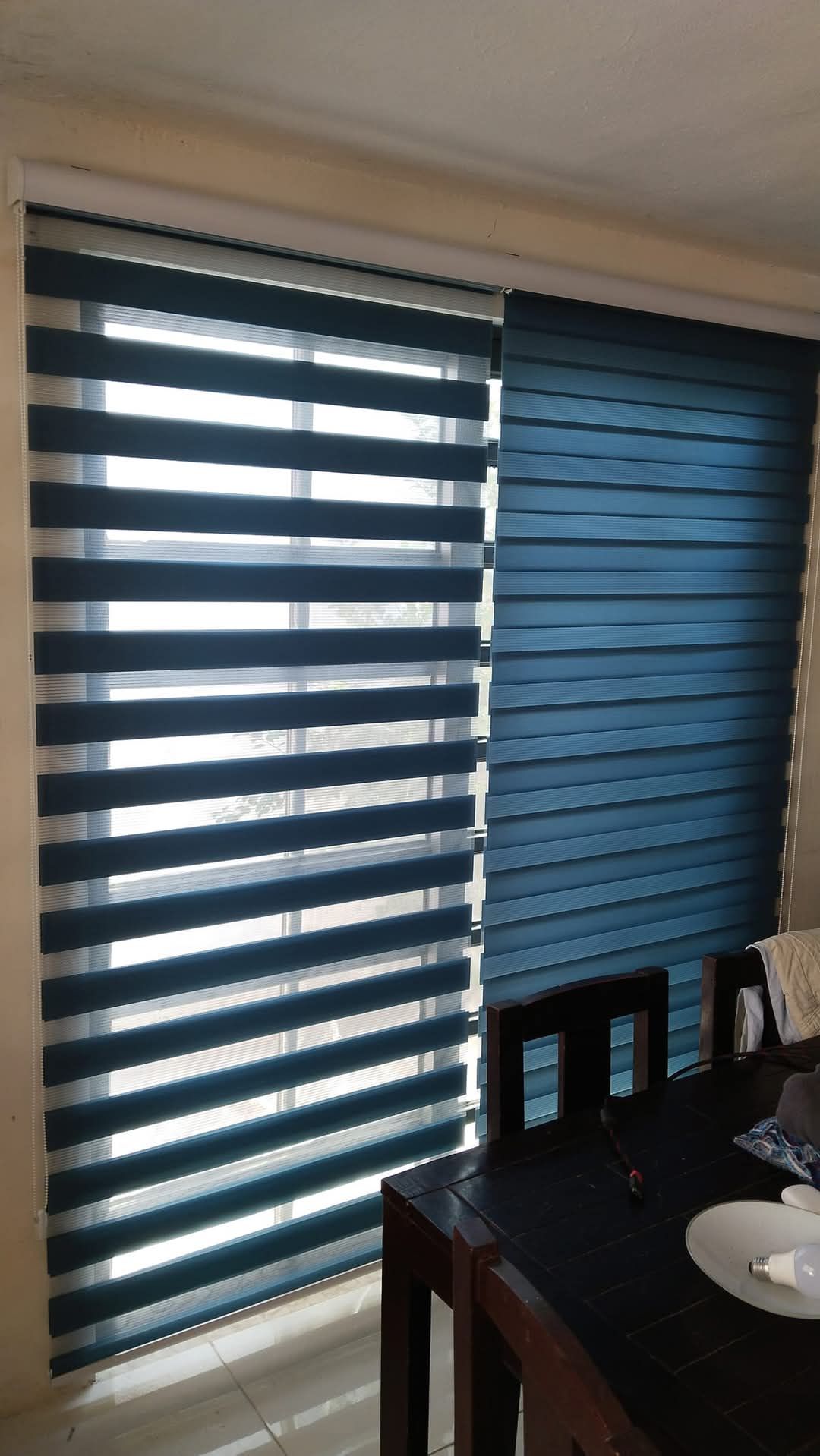 Un comedor con una mesa y sillas y una ventana con persianas azules.