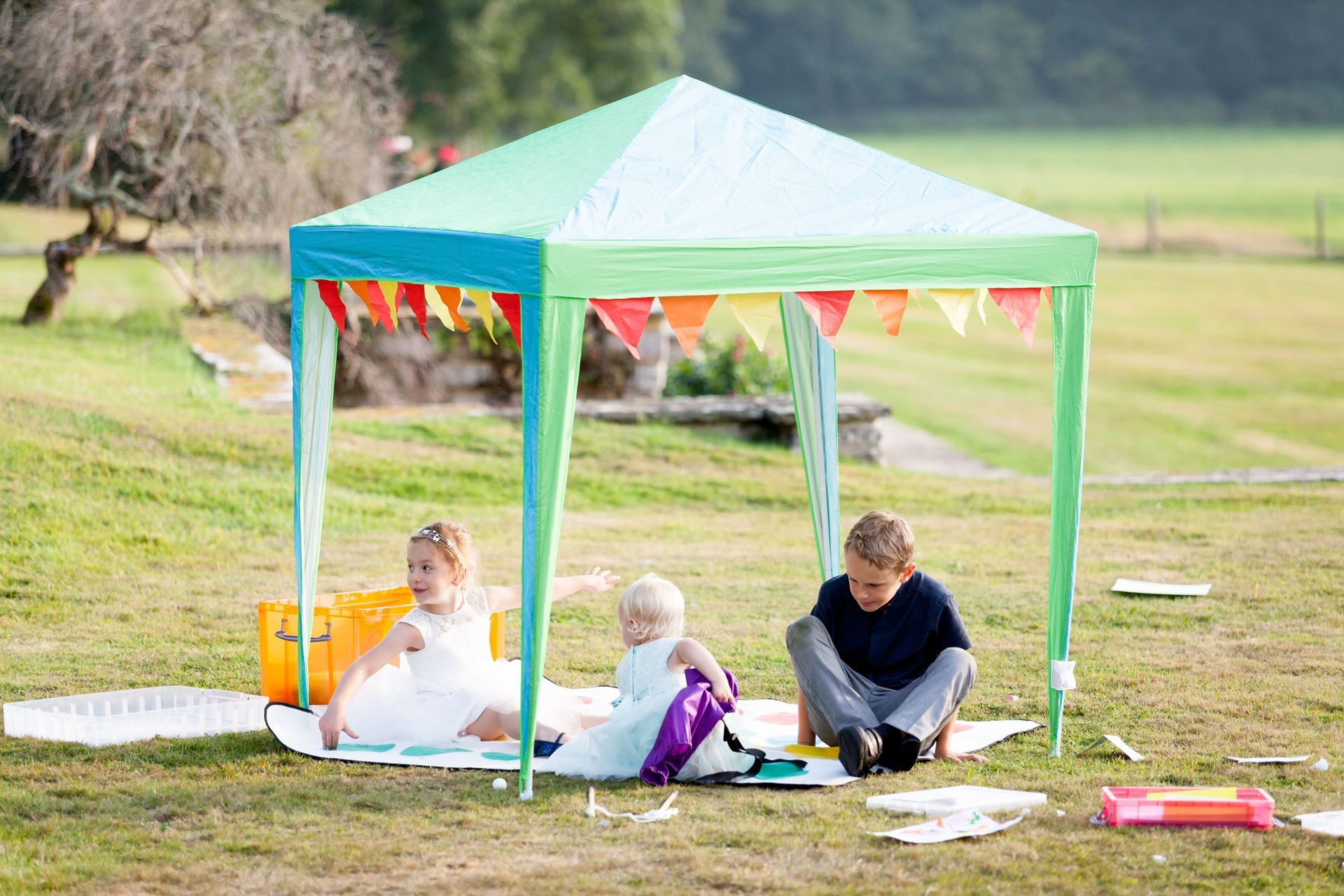 a group of children are sitting under a tent in the grass .