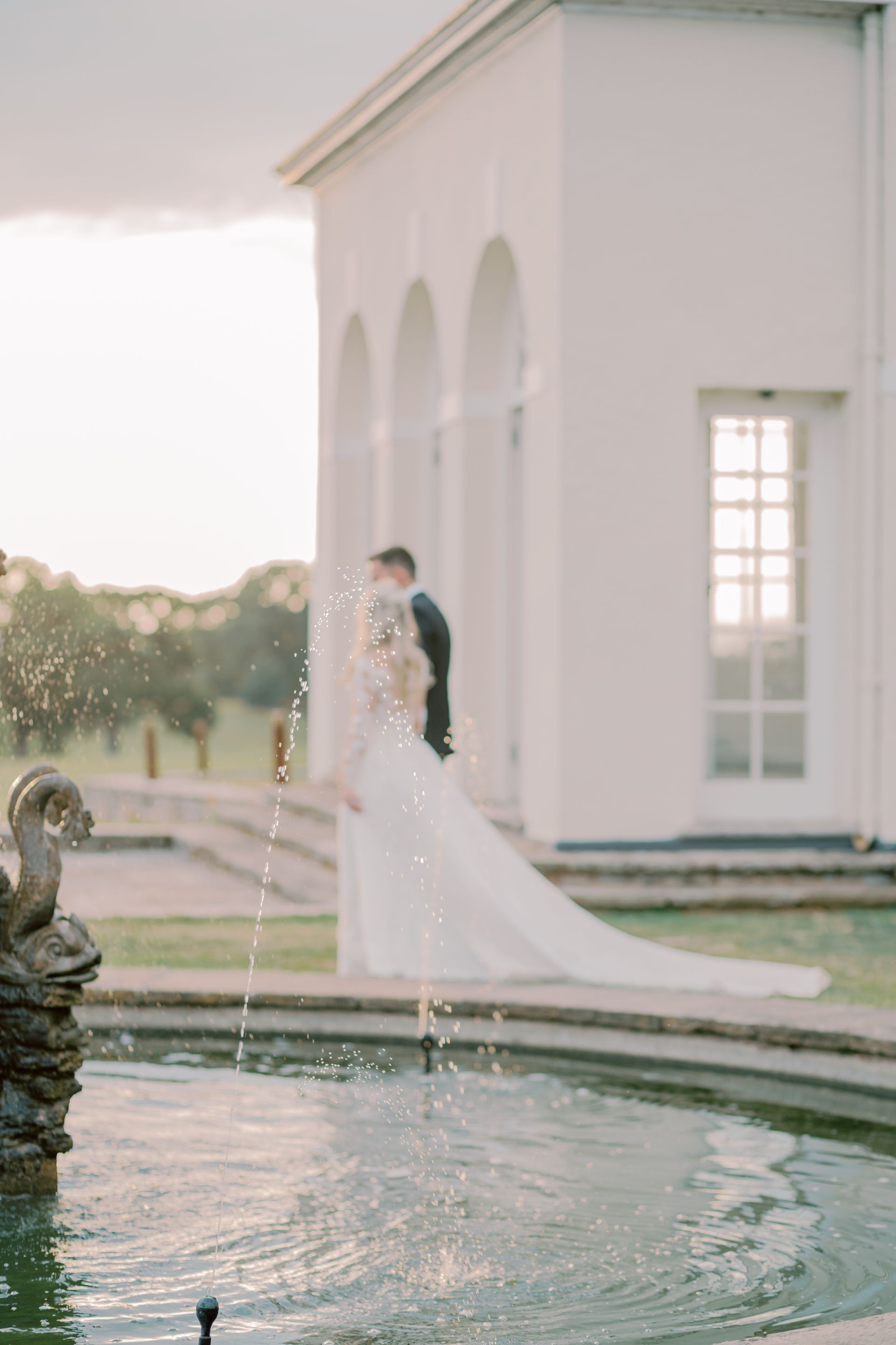a bride and groom are kissing in front of a fountain .