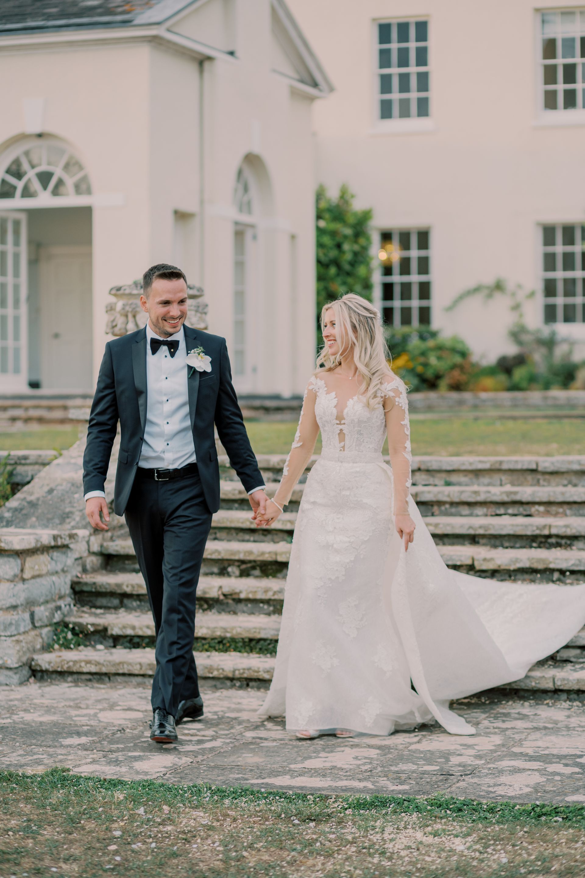 a bride and groom are walking down stairs holding hands in front of a white building .