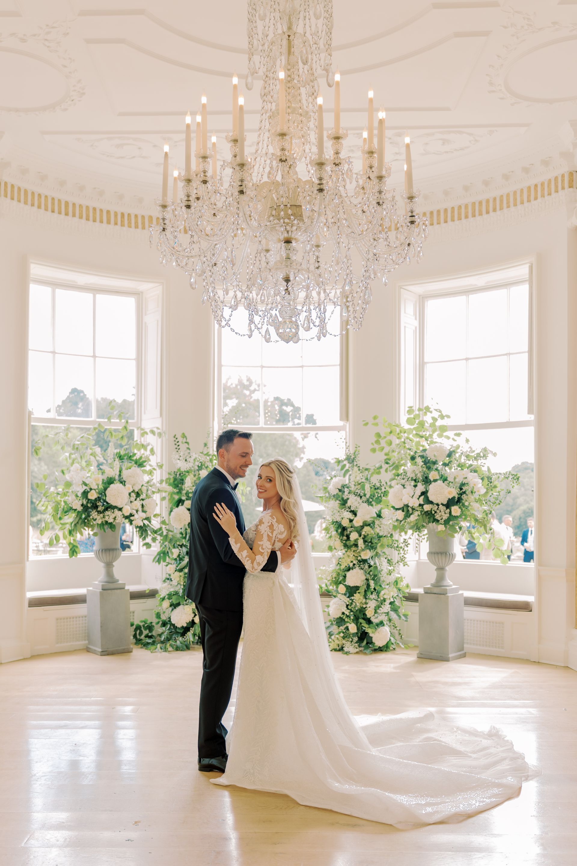 a bride and groom are standing in front of a chandelier in a room .