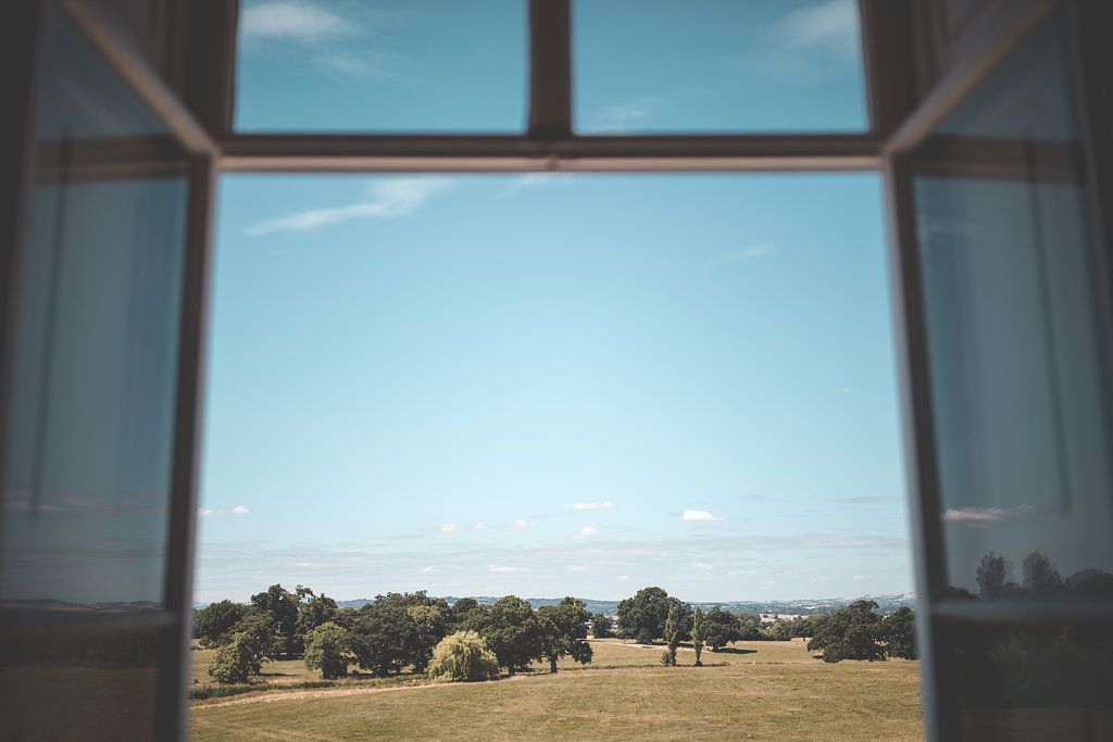 a view of a field and trees through an open window .