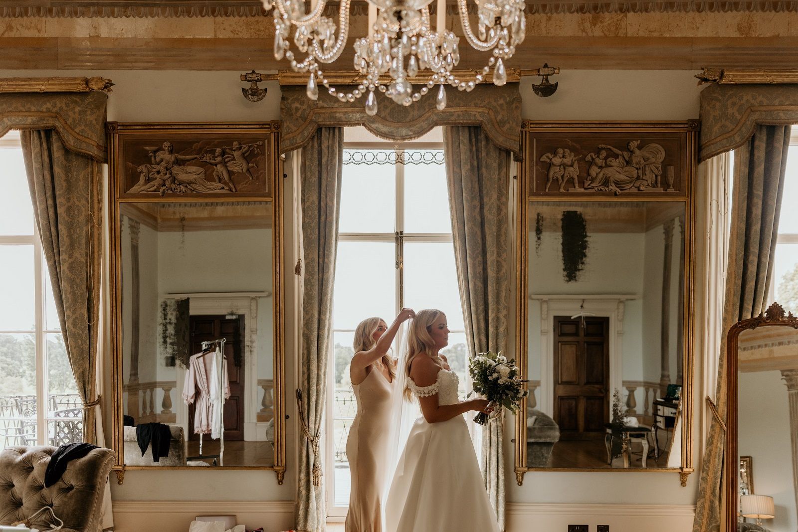 a bride and her mother are standing in front of a large mirror in a room .