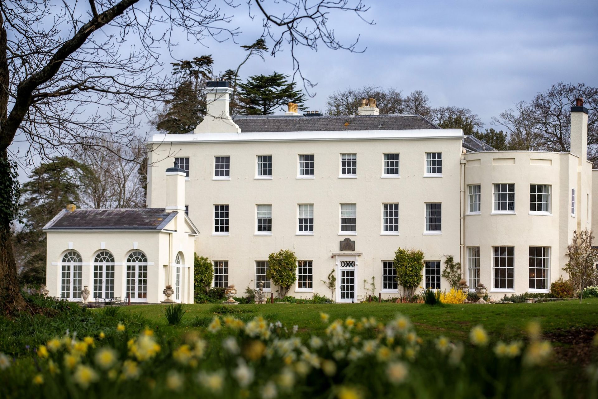 a large white house sits in the middle of a field of flowers