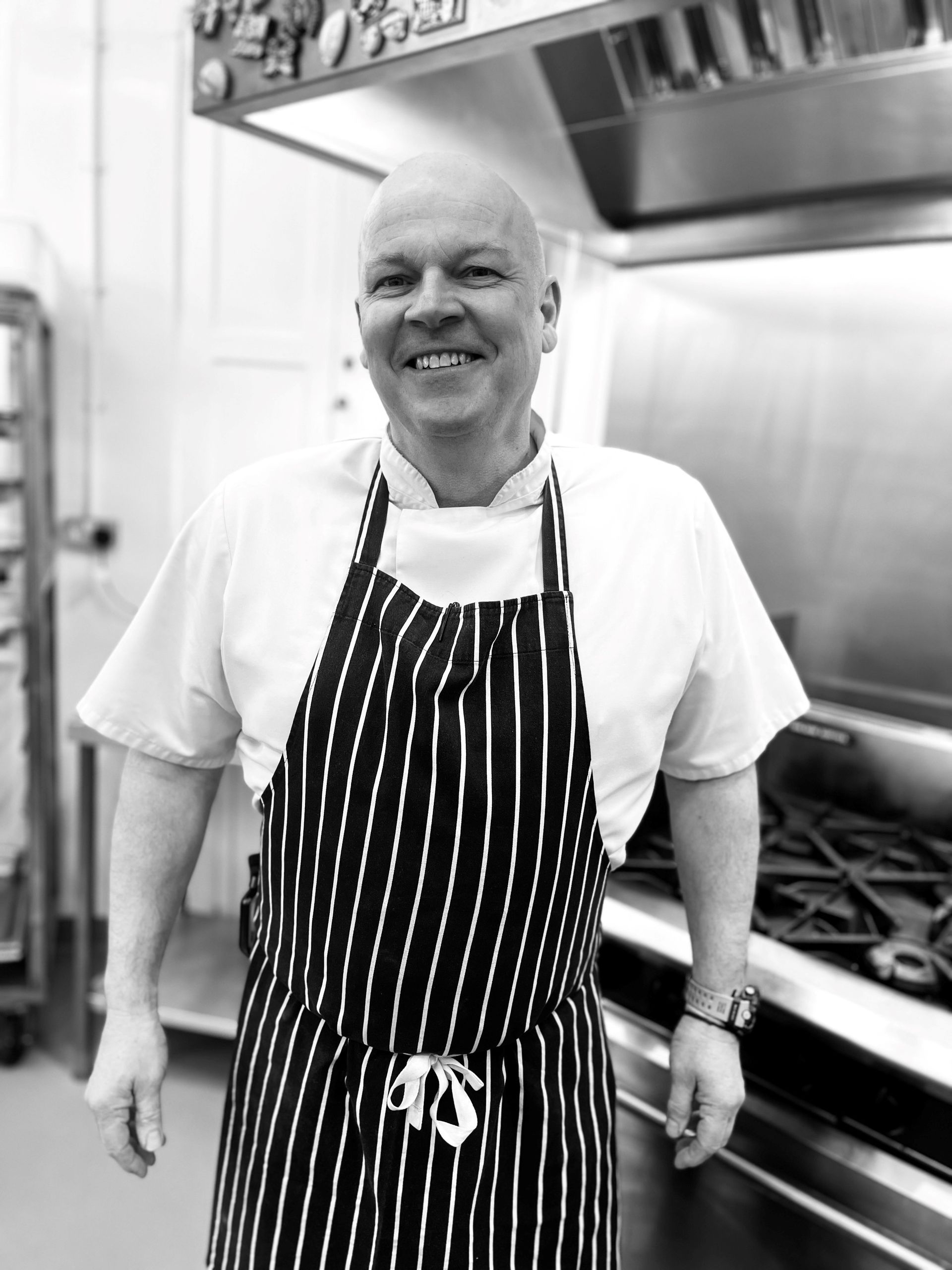 a man in an apron is pouring something into a bowl in a kitchen .