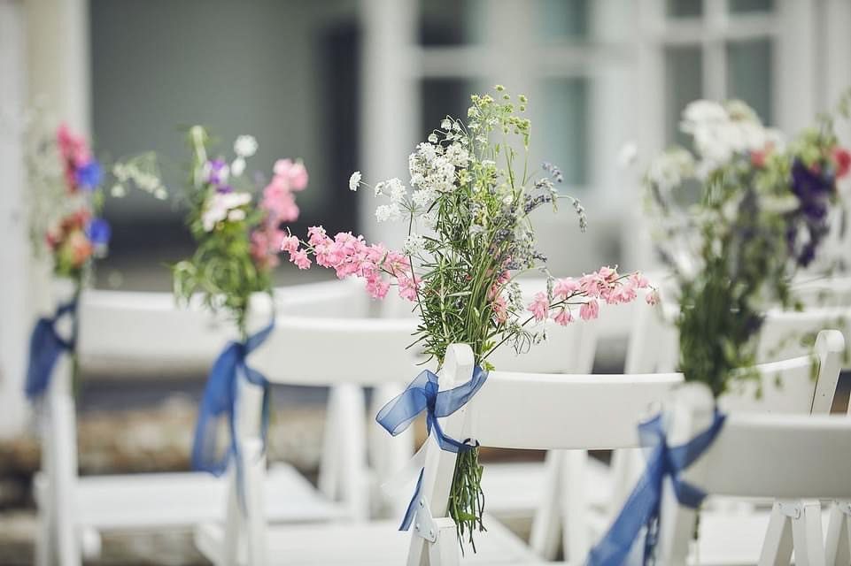 a row of white chairs decorated with flowers and blue ribbons .