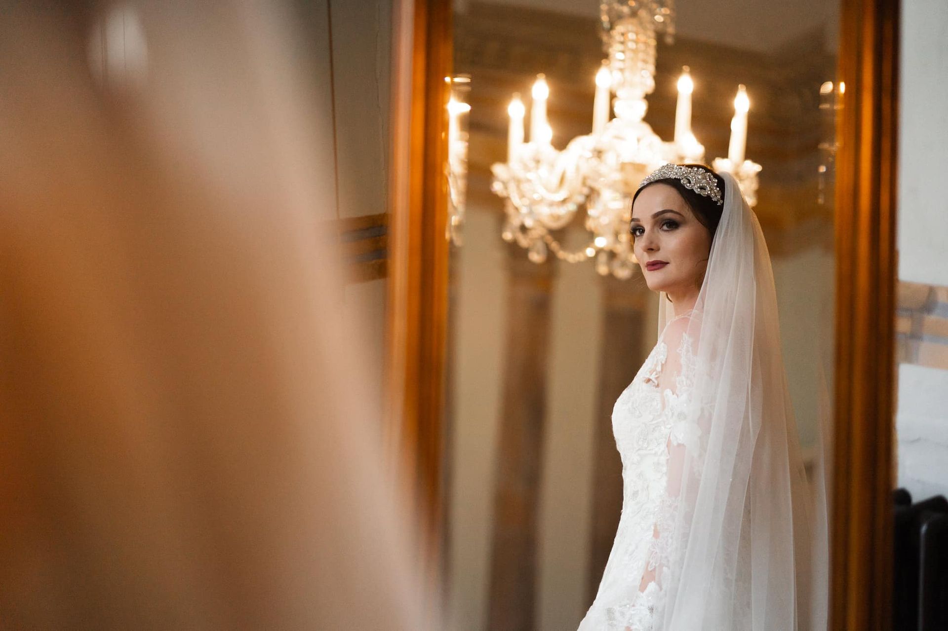 a bride in a wedding dress and veil is standing in front of a mirror .