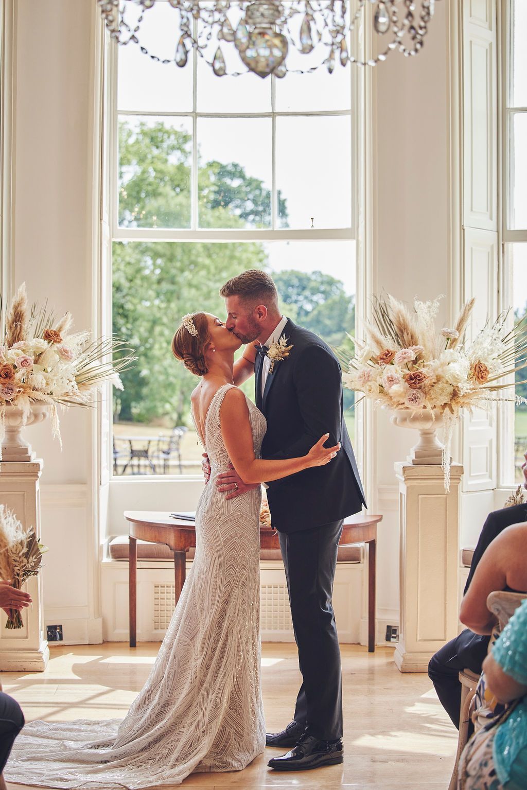a bride and groom are kissing during their wedding ceremony in front of a large window .