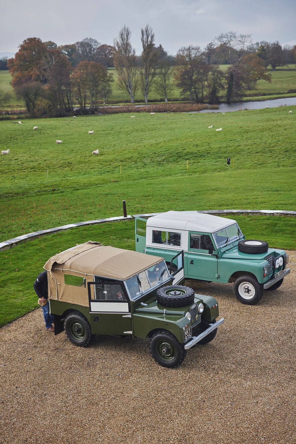 two old land rovers are parked next to each other in a gravel driveway .