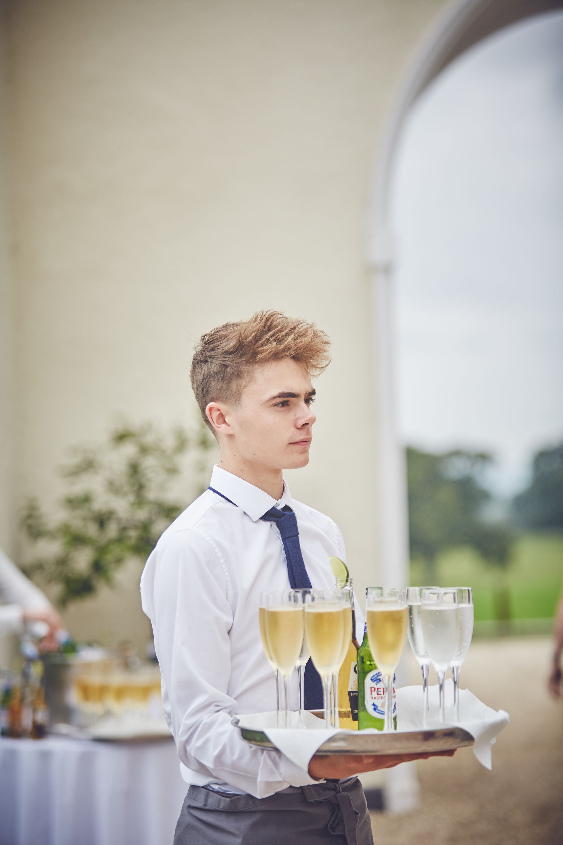 a man is holding a tray of champagne glasses and water.