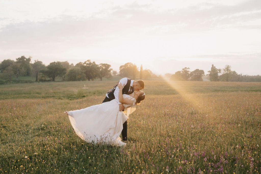 a bride and groom are standing in a grassy field .