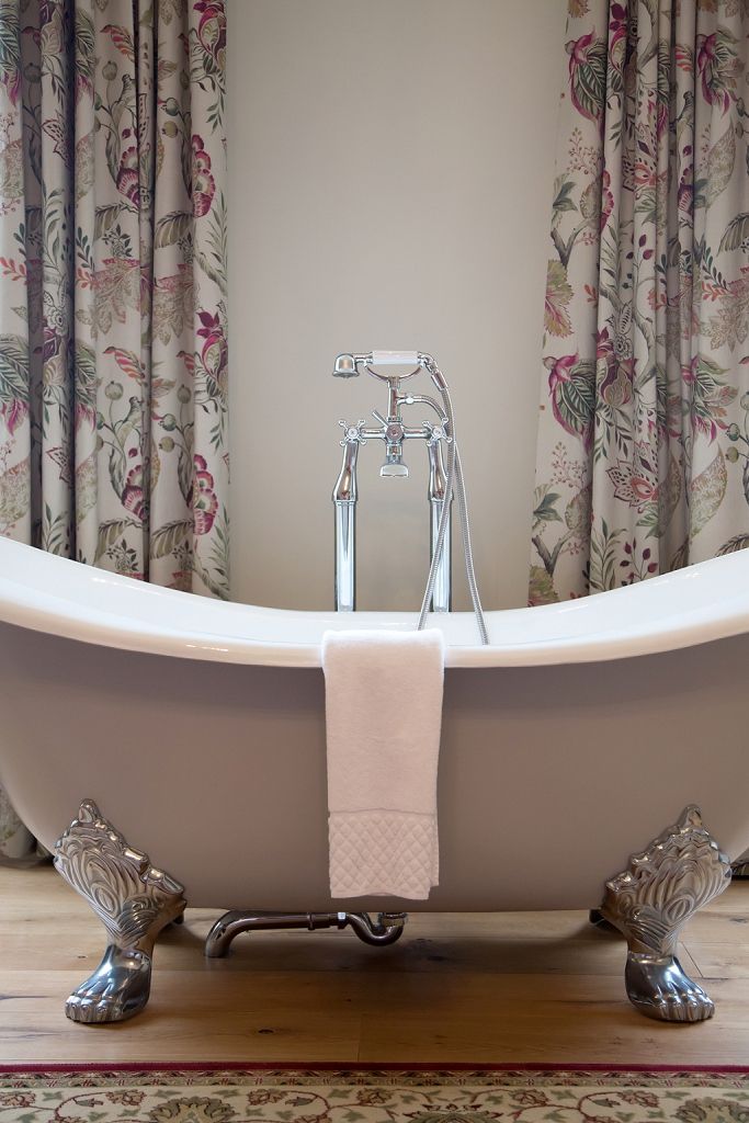 a bathtub in a bathroom with floral curtains and a rug .