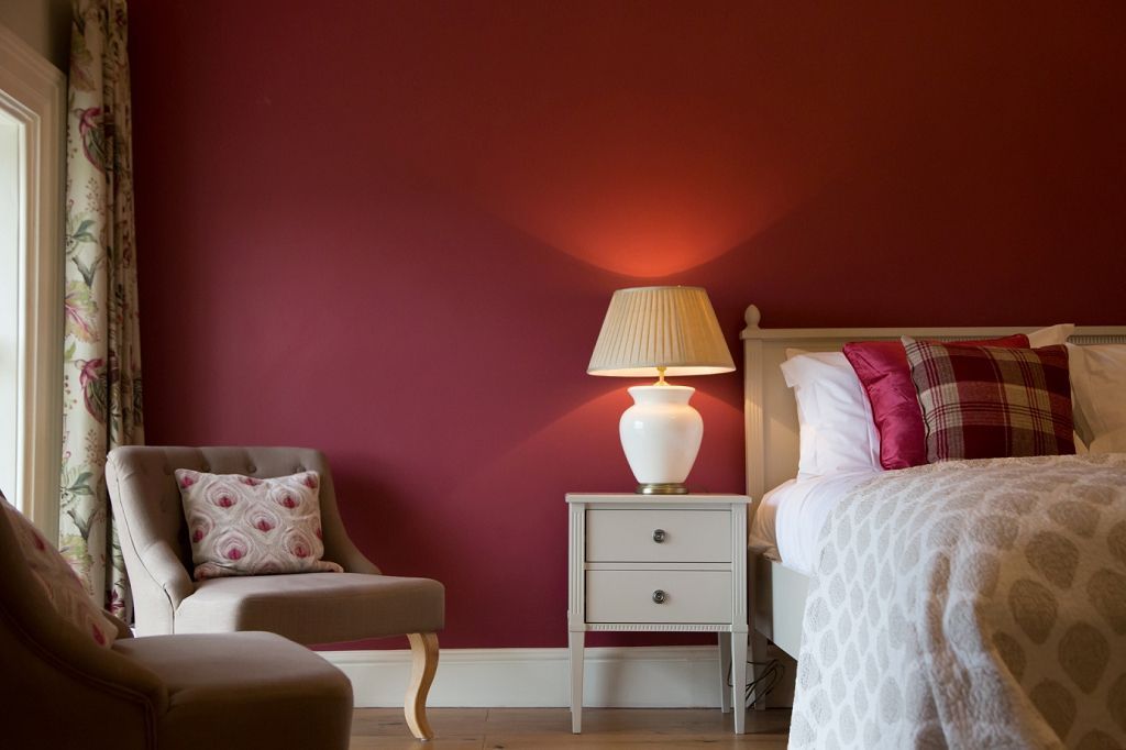 a bedroom with a bed , chair , nightstand , lamp and red walls .
