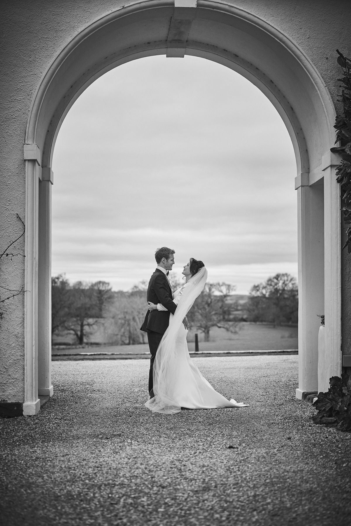 a black and white photo of a bride and groom walking in a field .