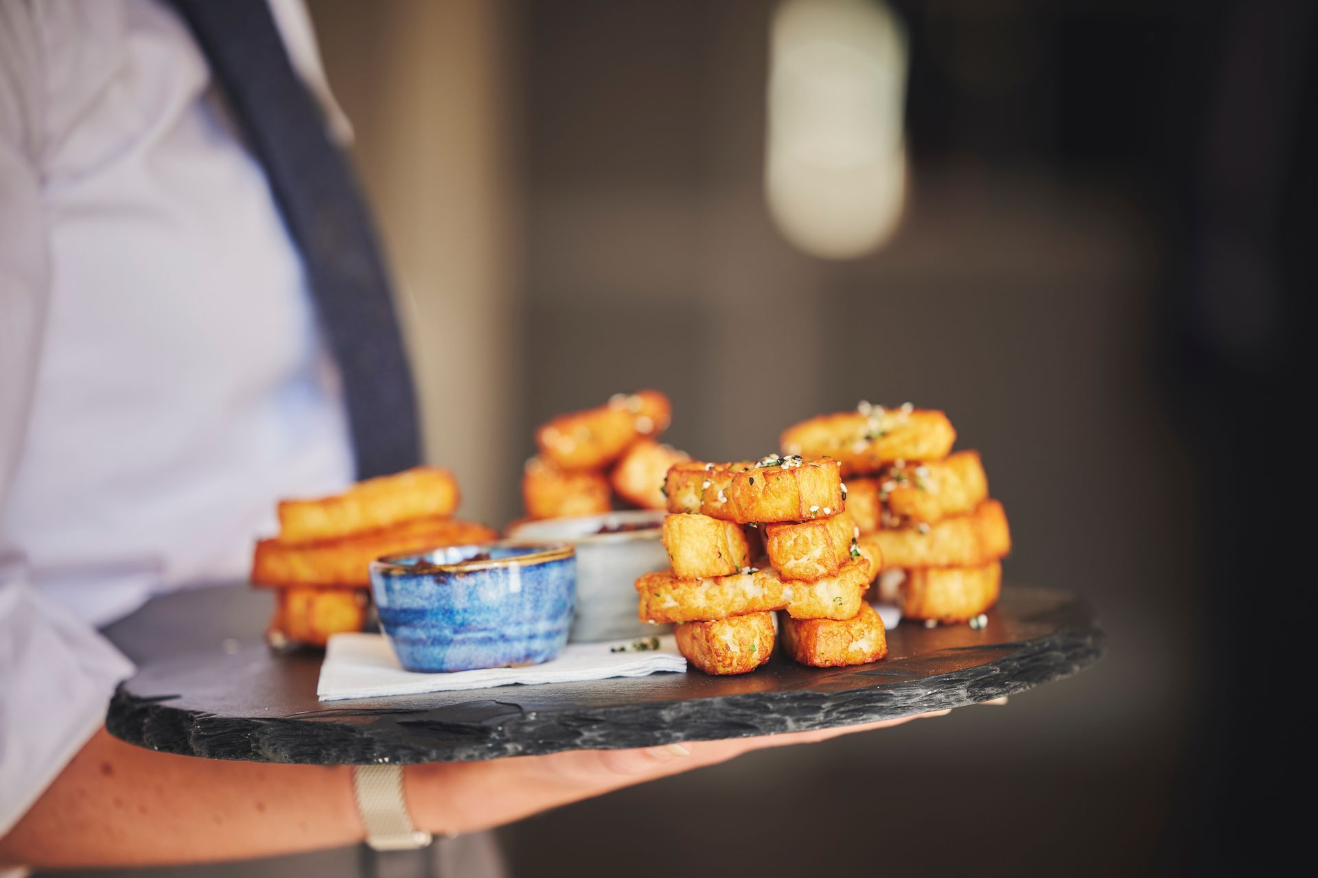 a waiter is holding a tray of onion rings and dipping sauce .