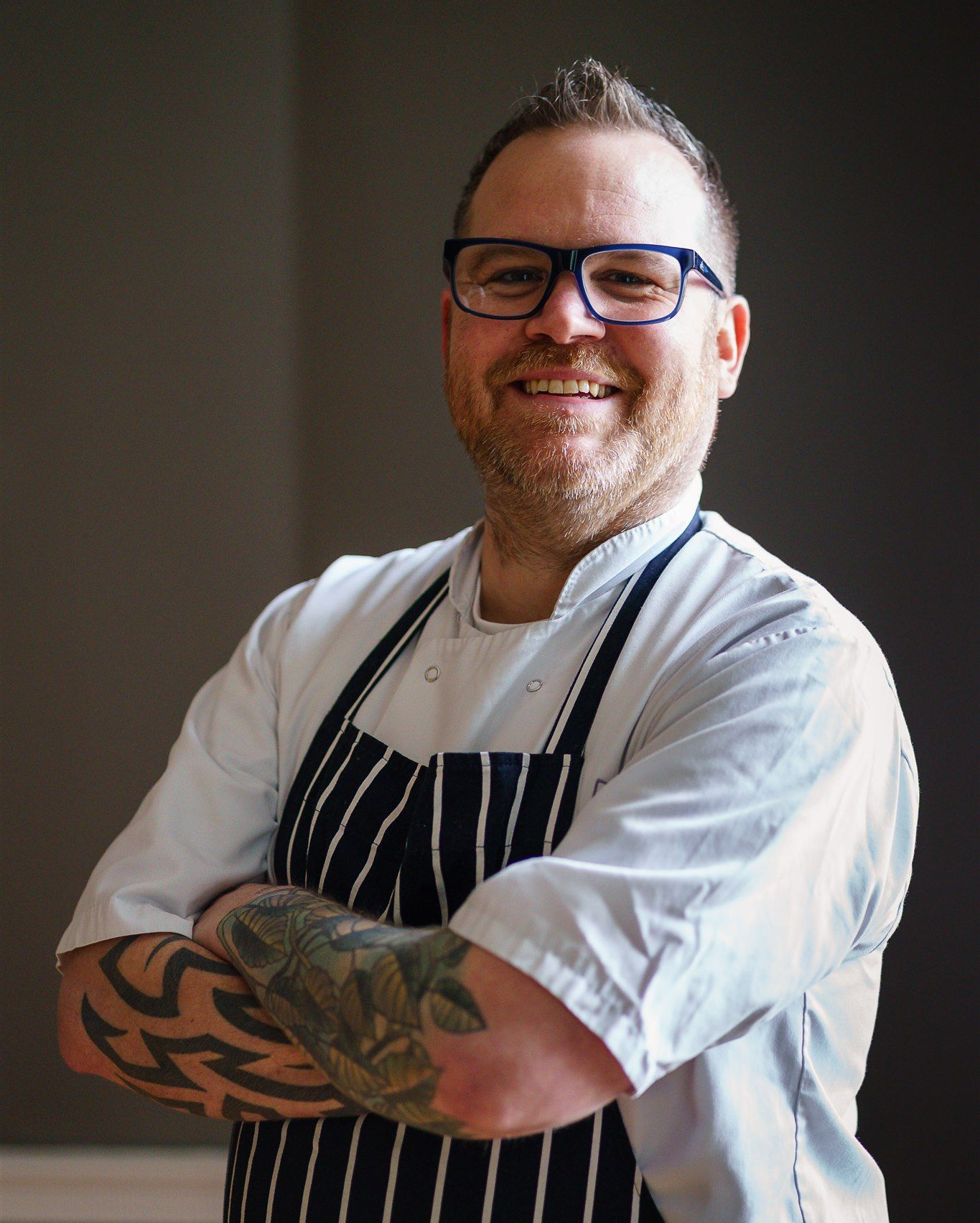 a man in an apron is standing in front of a door with his arms crossed .
