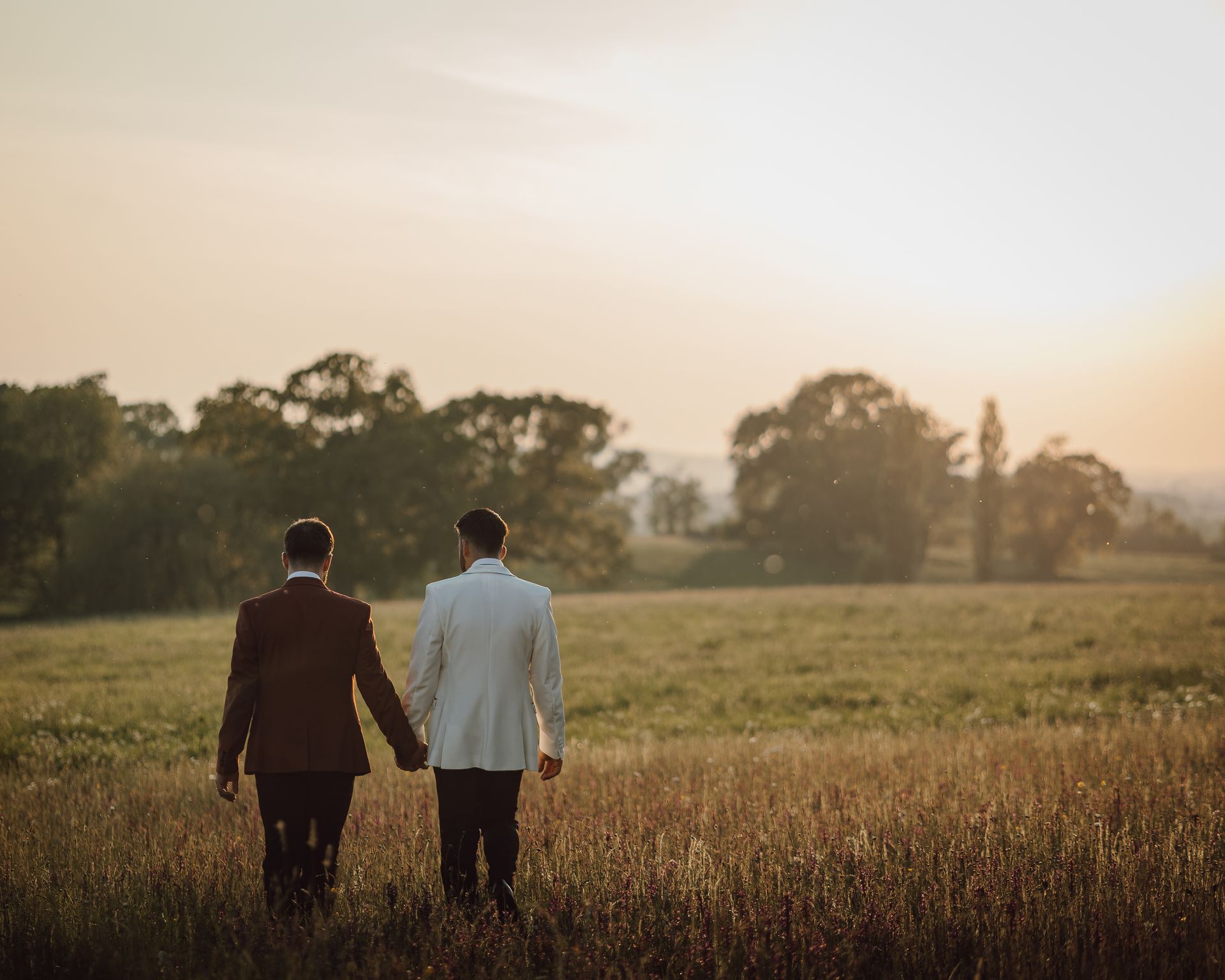 two men are walking through a field holding hands .