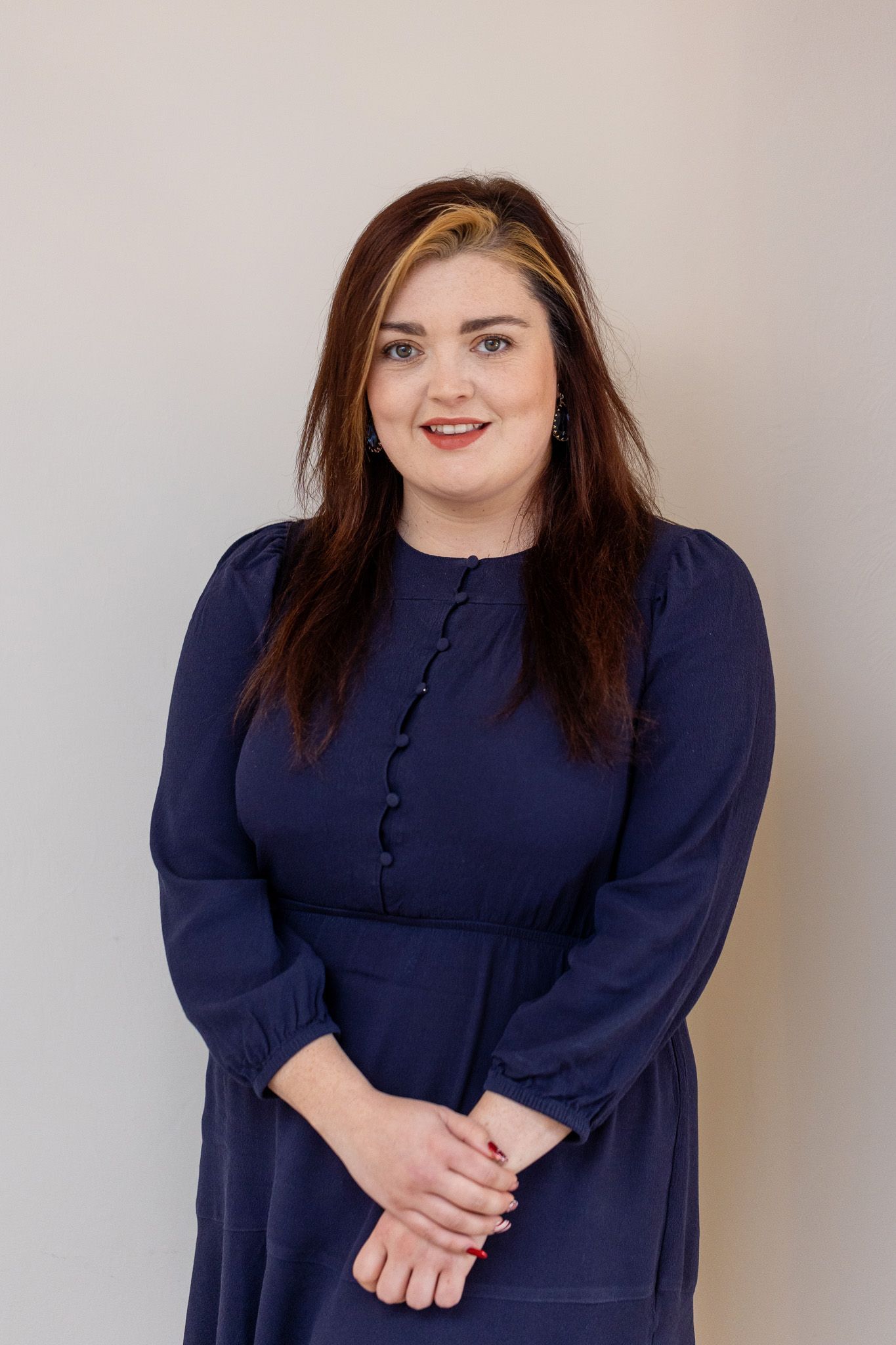 a woman in a blue dress is standing with her hands folded in front of a white wall .