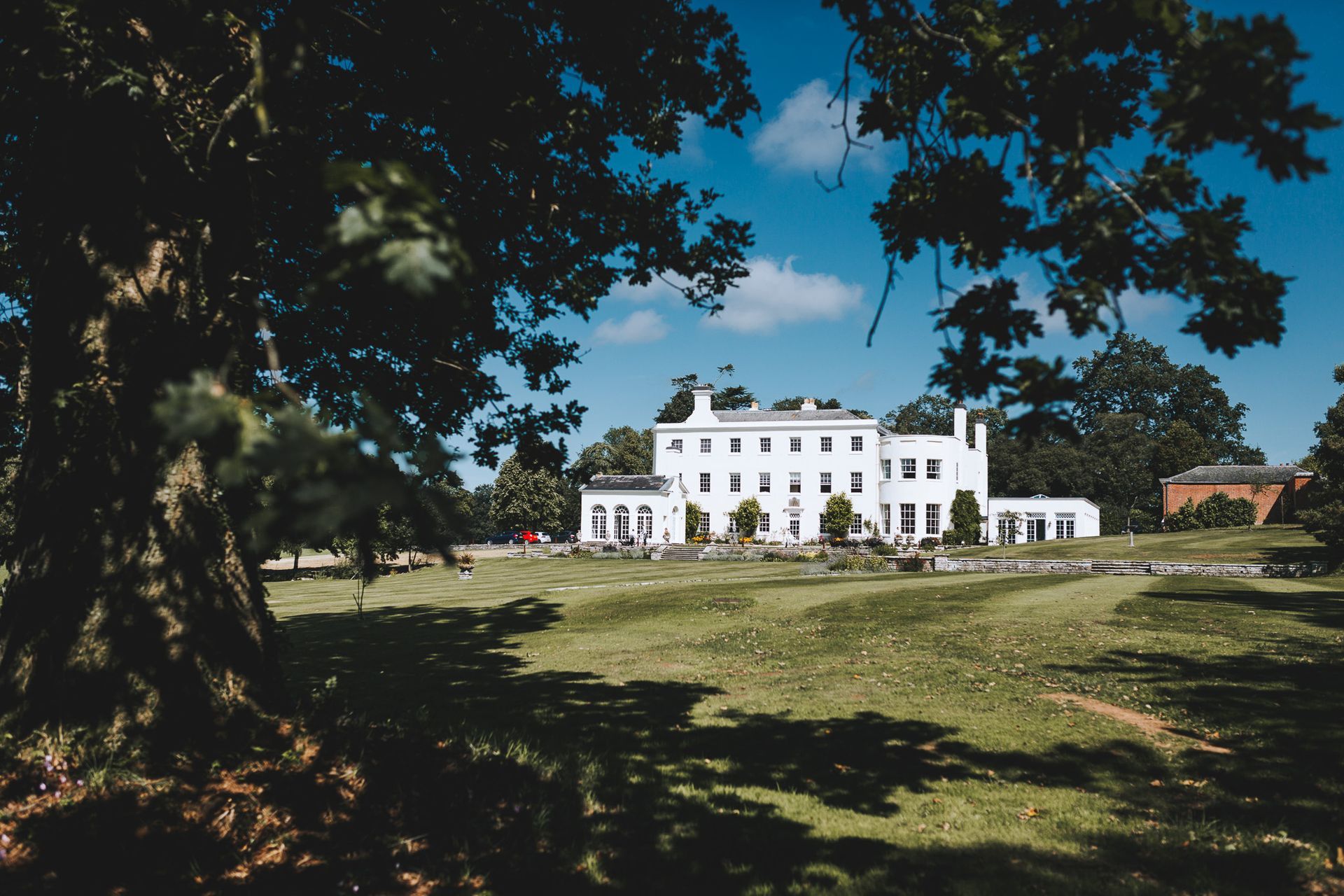 a large white house is sitting on top of a lush green field surrounded by trees .