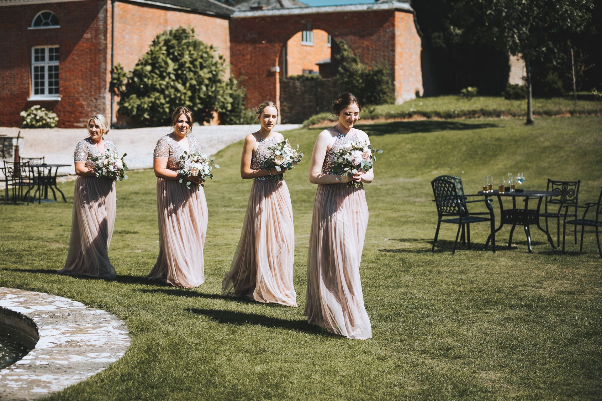 a group of bridesmaids are walking down a lush green field holding bouquets of flowers .