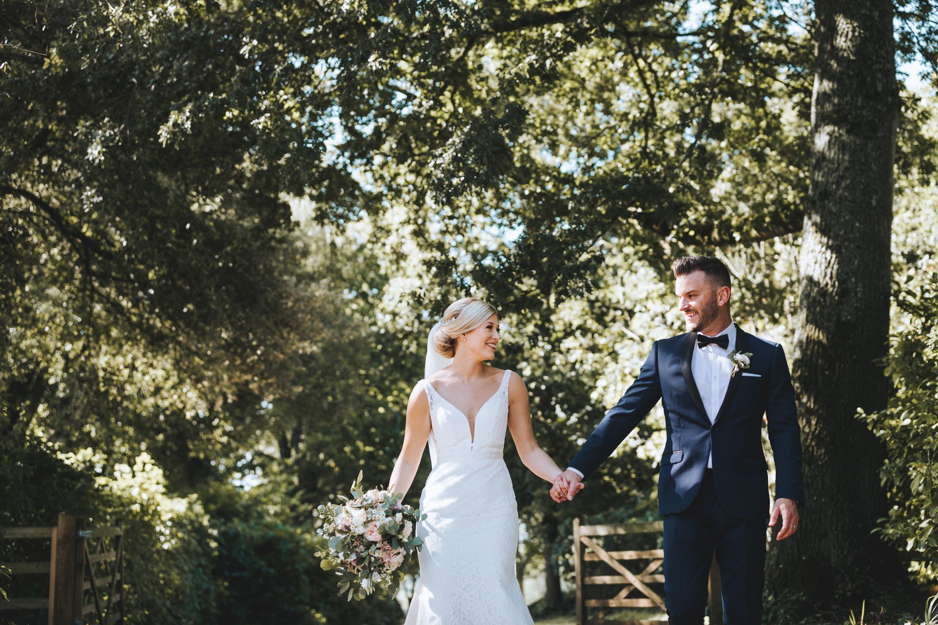 a bride and groom are holding hands while walking through a forest .
