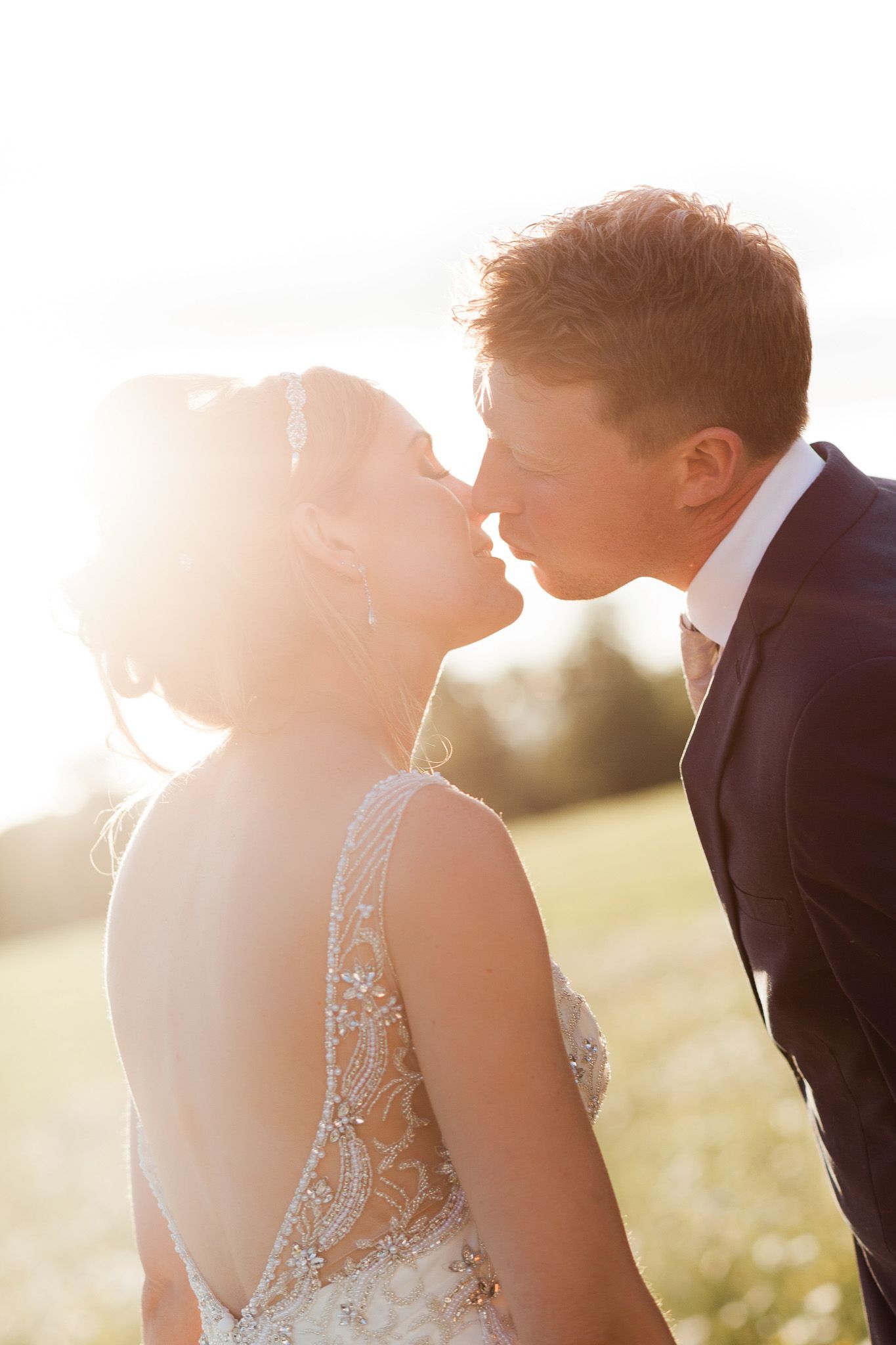 a bride and groom are kissing in a field at their wedding.