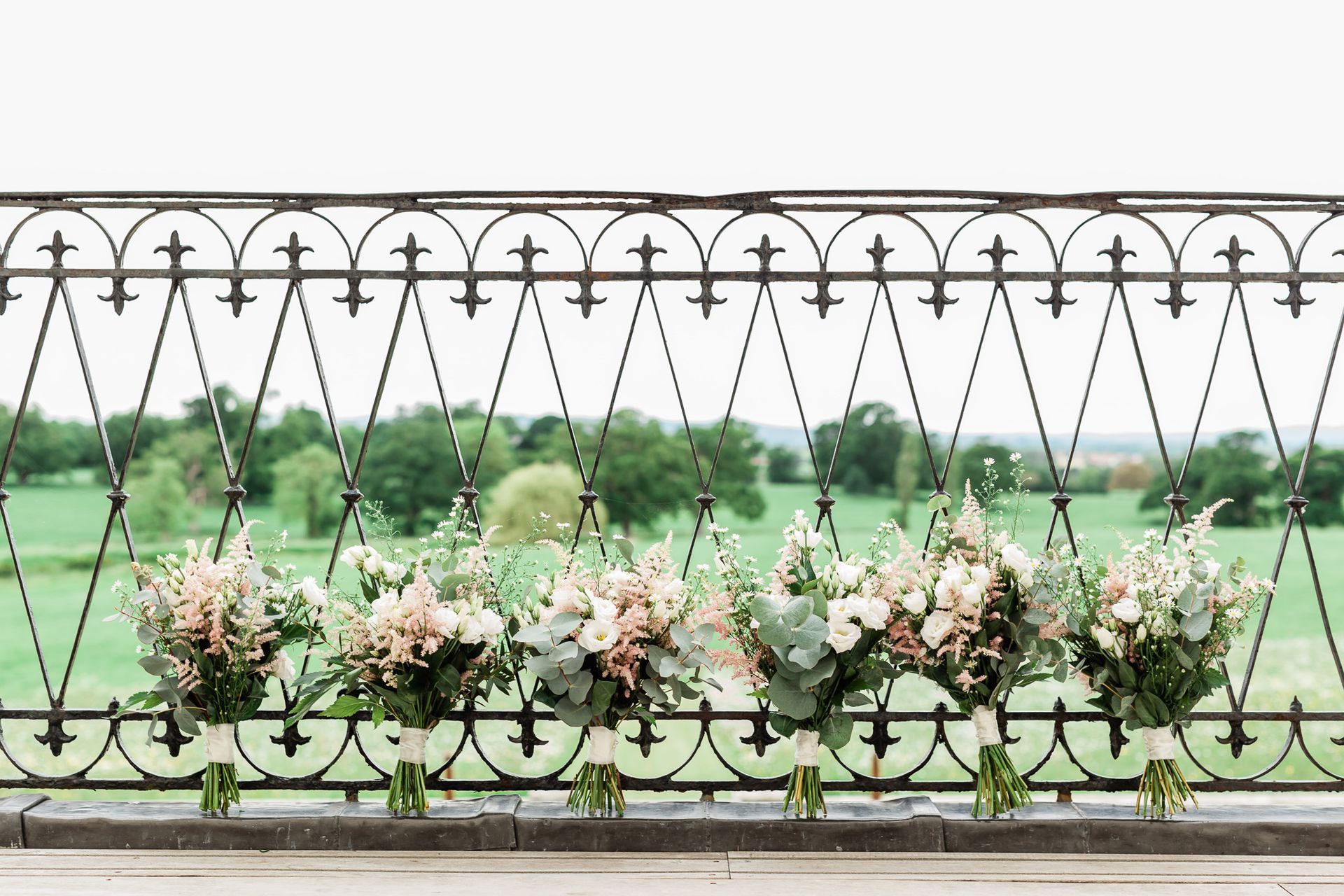 a row of bouquets of flowers hanging from a wrought iron railing.