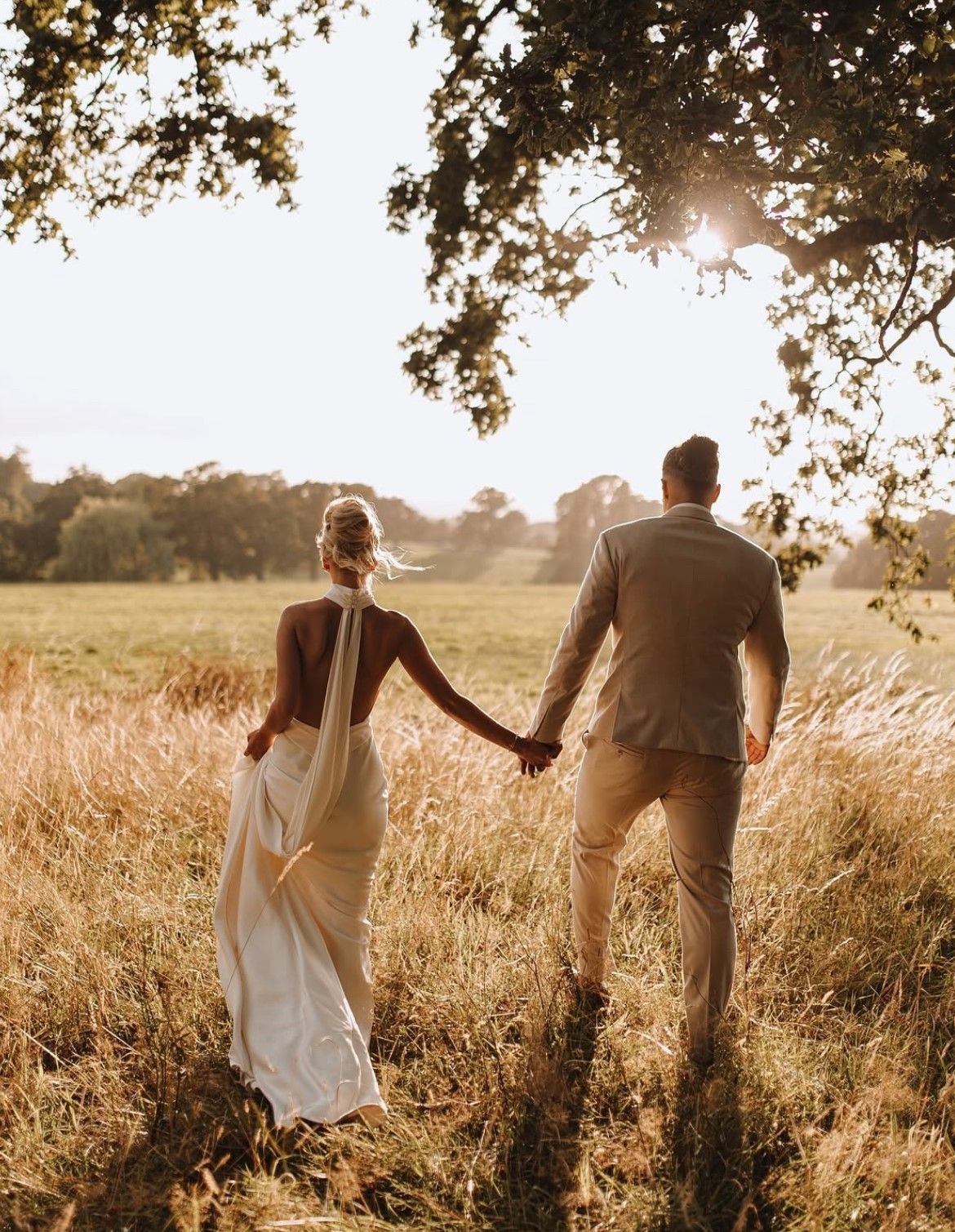 a bride and groom are standing in a grassy field .