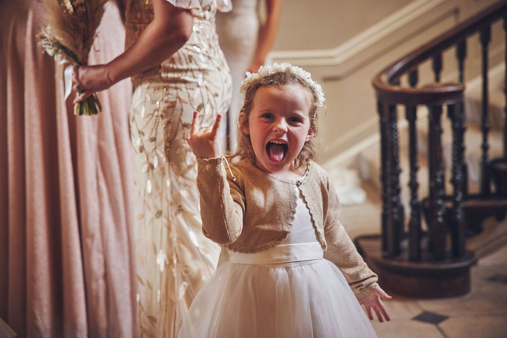 a little girl in a flower girl dress is making a rock sign .