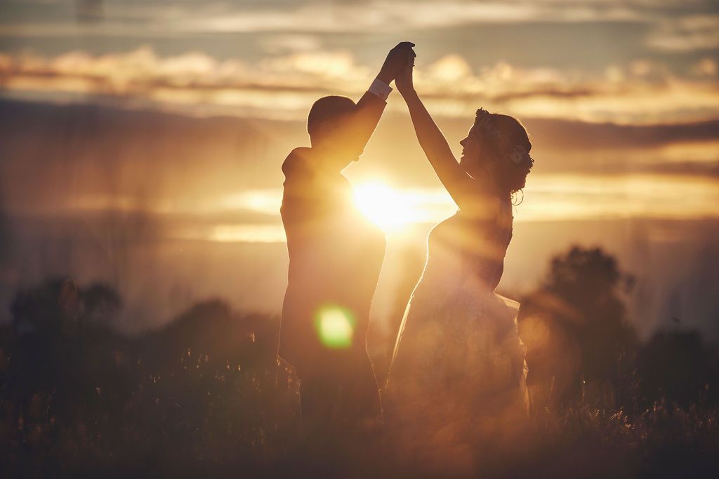 a bride and groom are dancing in a field at sunset .