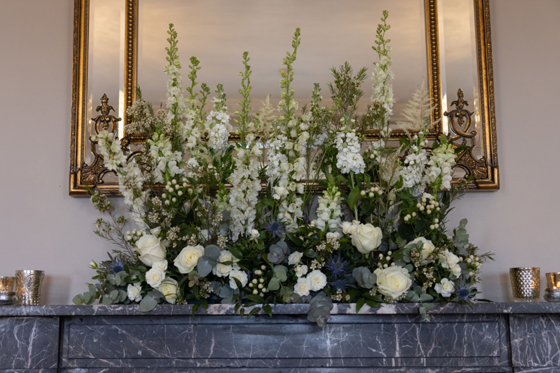 a mantle decorated with white flowers and greenery in front of a mirror .
