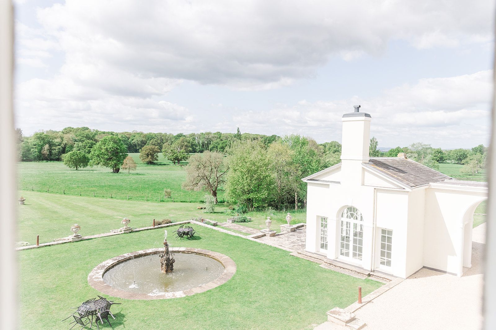 an aerial view of a white house with a fountain in the middle of a lush green field. wedding venue in devon.