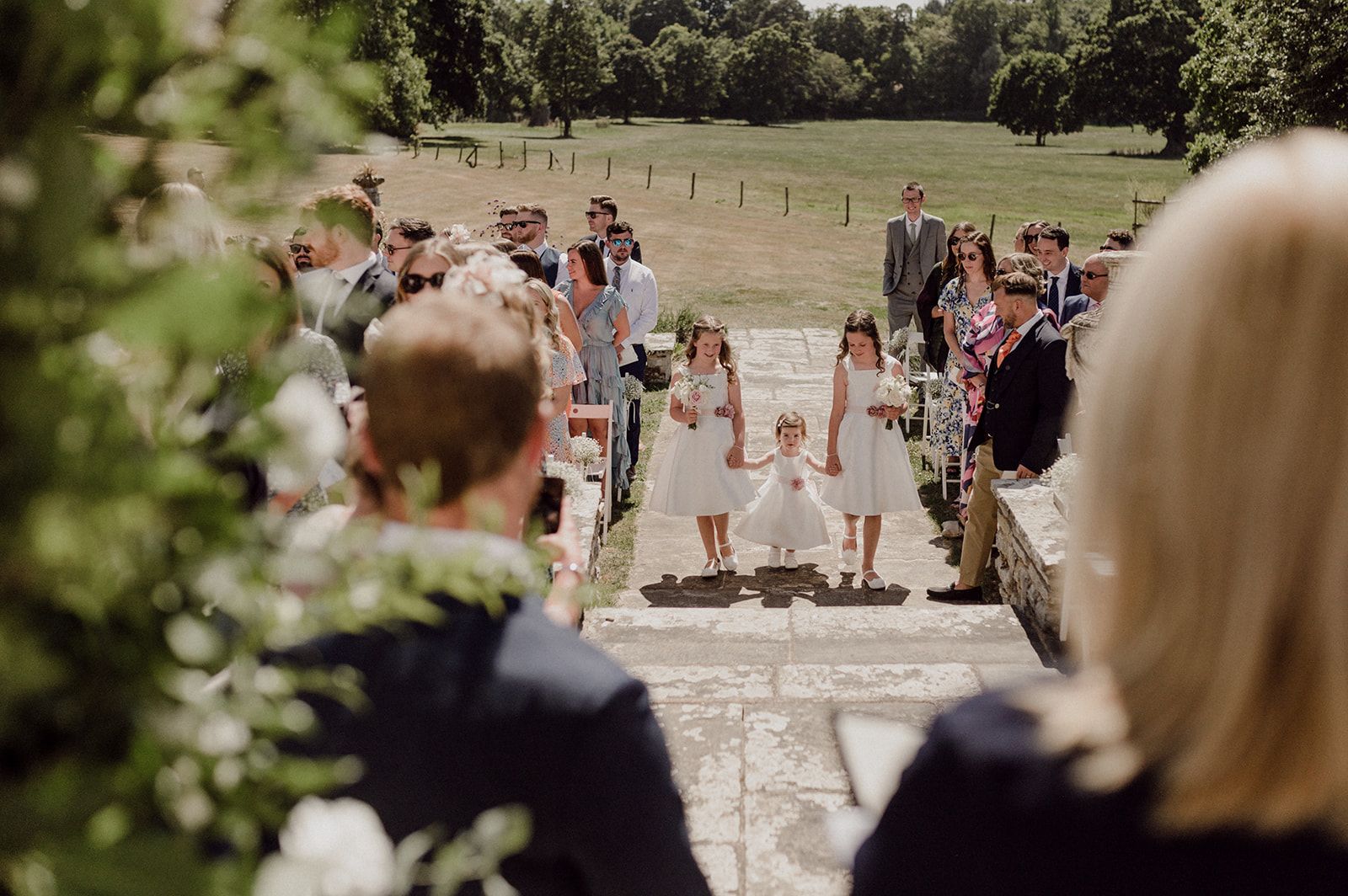 a group of people are watching a wedding ceremony with flower girls walking down the aisle .