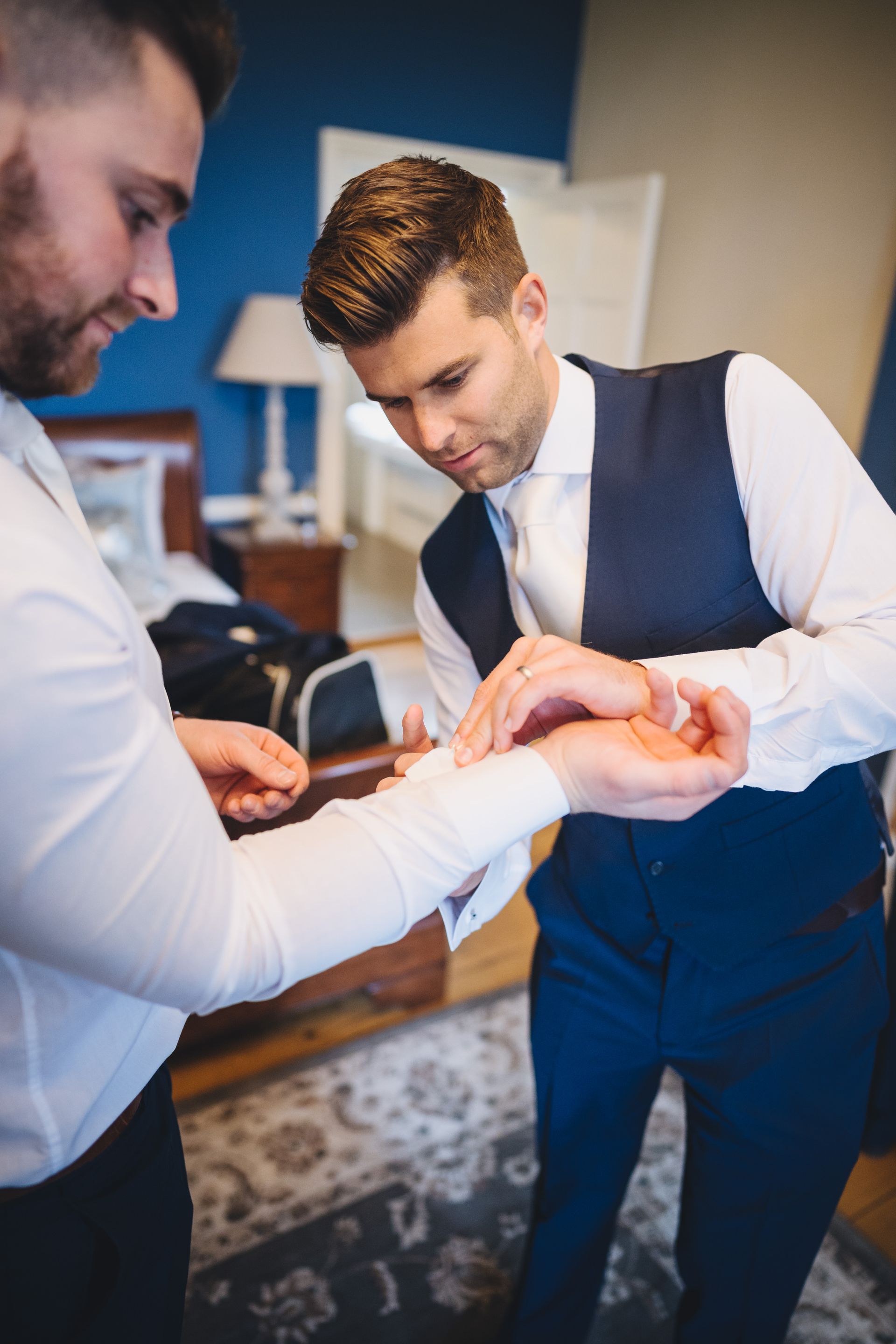 two men are getting ready for a wedding and putting on cufflinks .