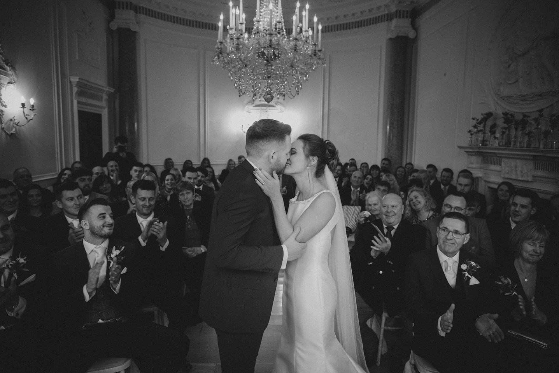 a black and white photo of a bride and groom kissing during their wedding ceremony .