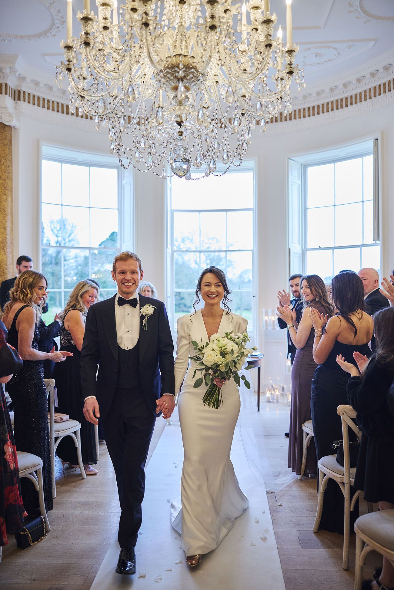 a black and white photo of a bride and groom walking in a field .