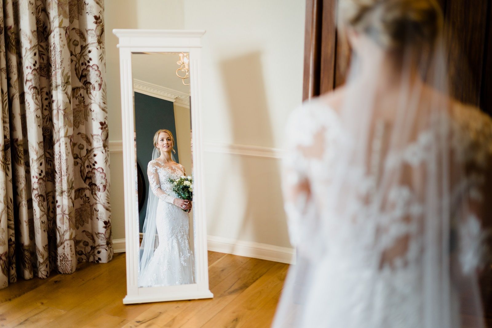 a bride is standing in front of a mirror holding a bouquet of flowers .