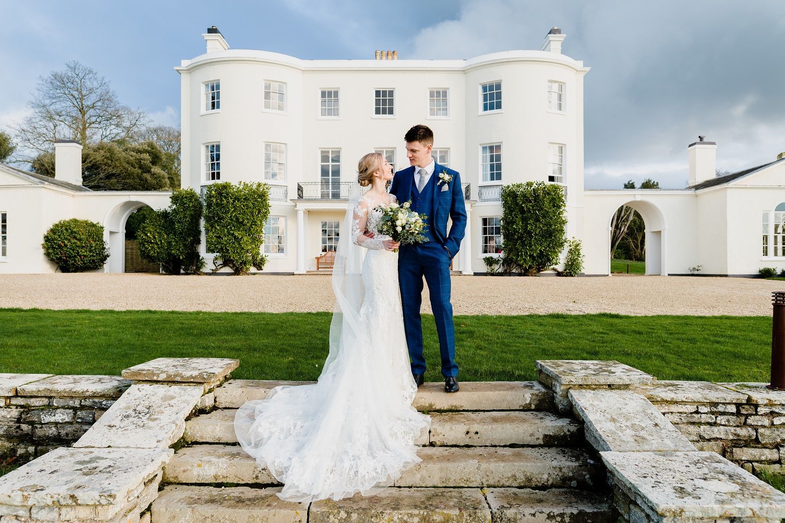 a bride and groom are posing for a picture in front of a large white building .