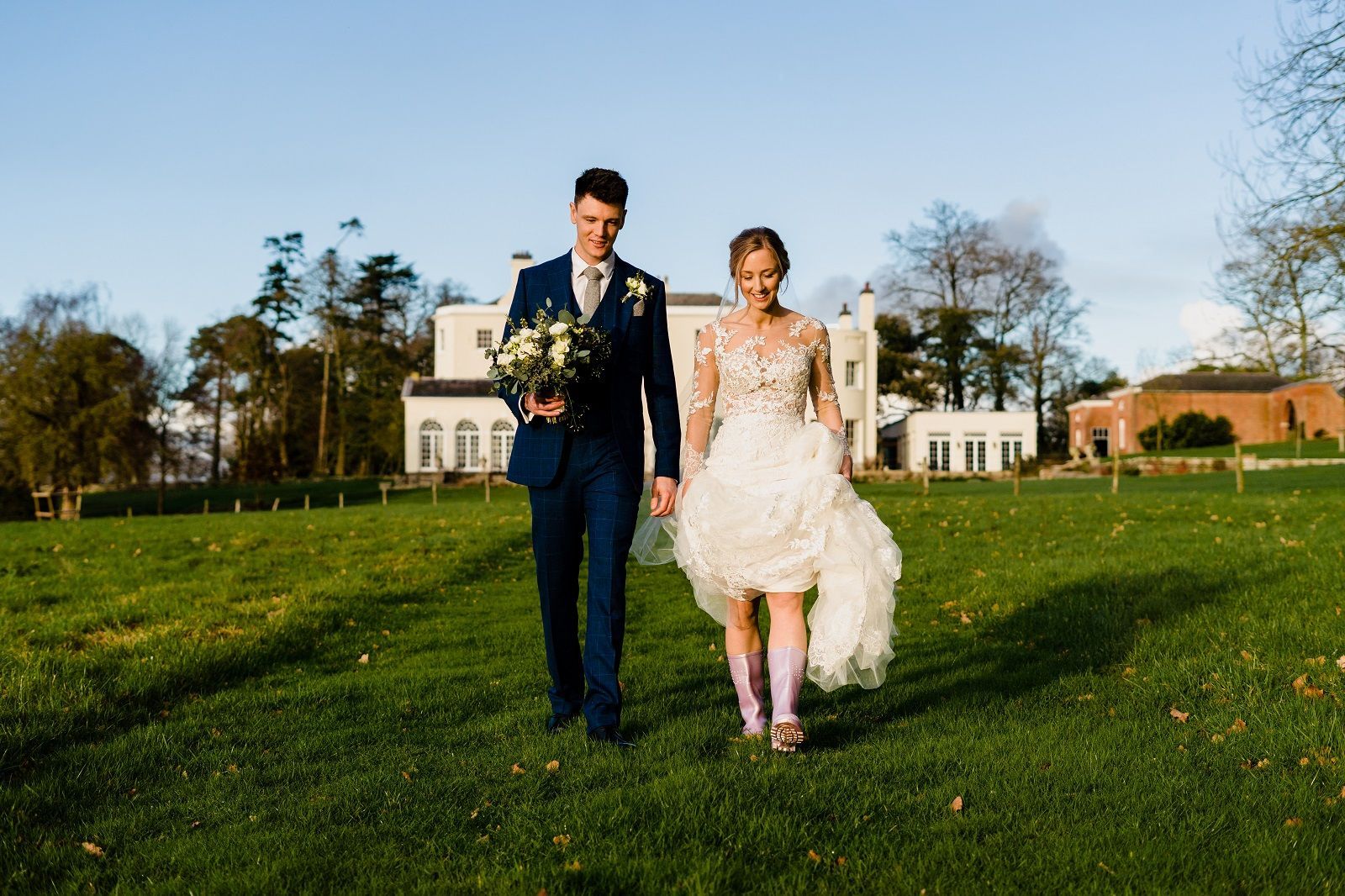 a bride and groom are walking through a grassy field holding hands .