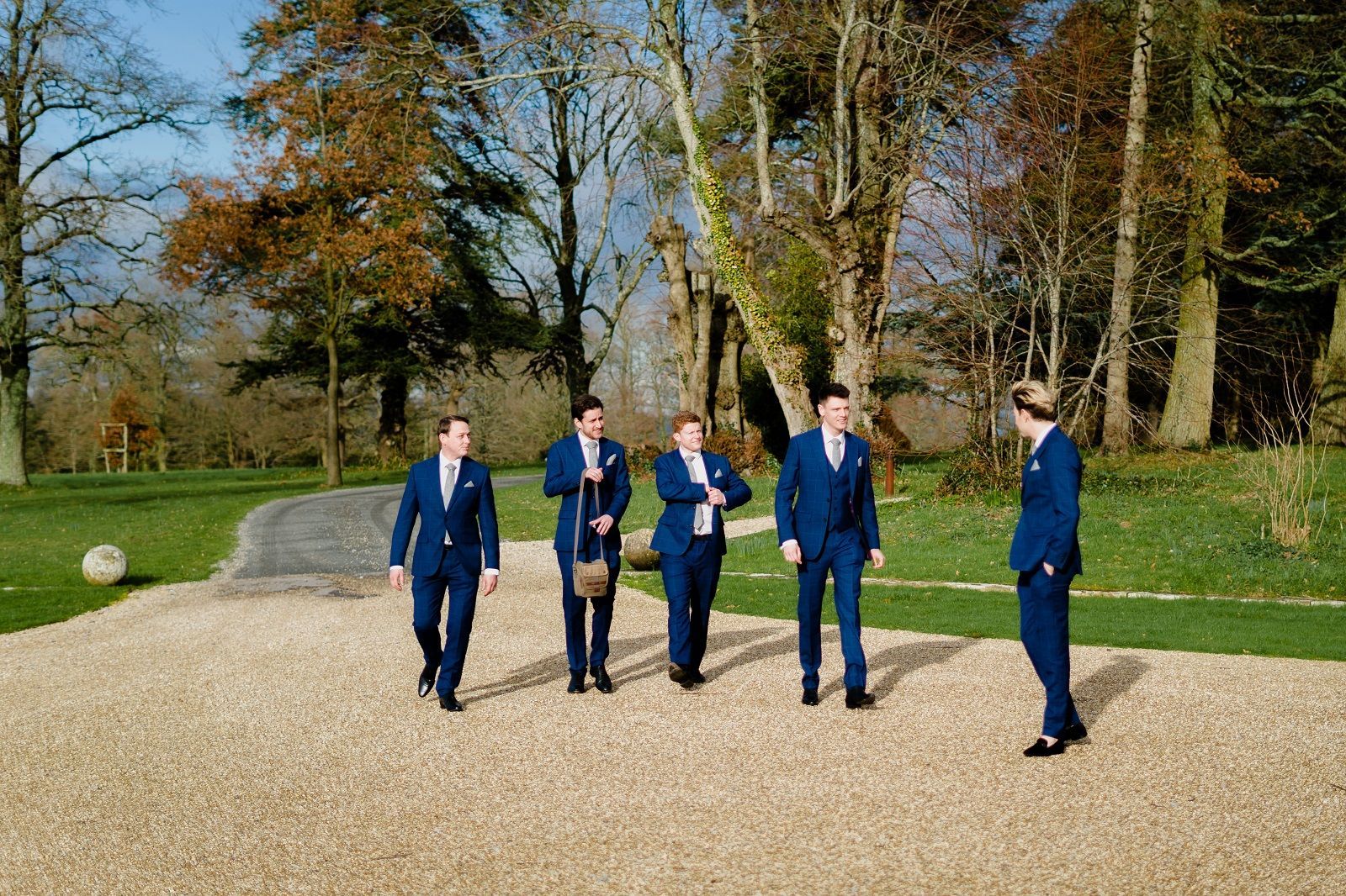 a group of men in suits are walking down a gravel road .